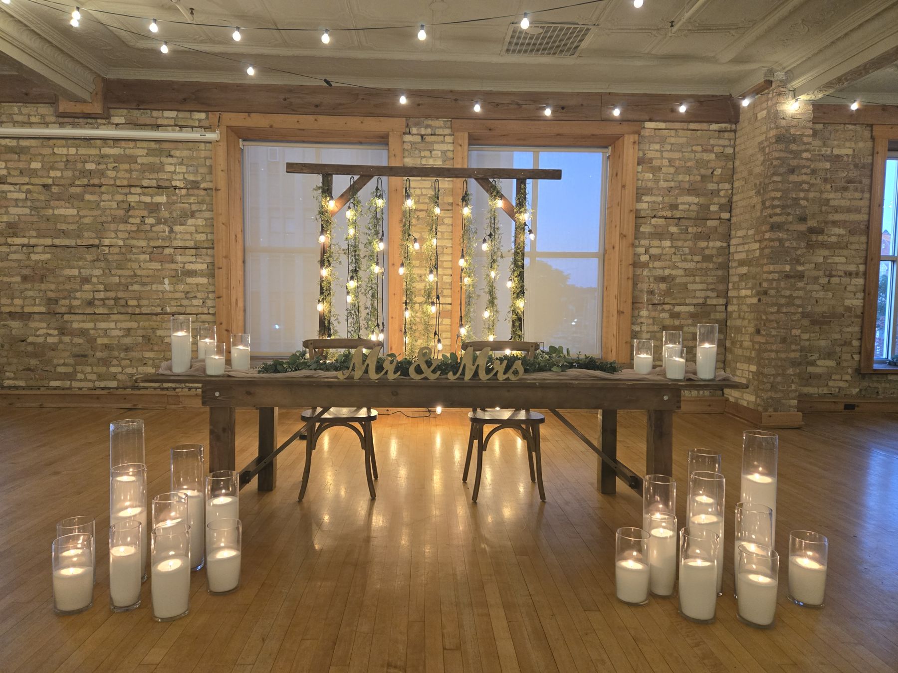 A wooden sweetheart table with layered glass hurricanes on the table and floor