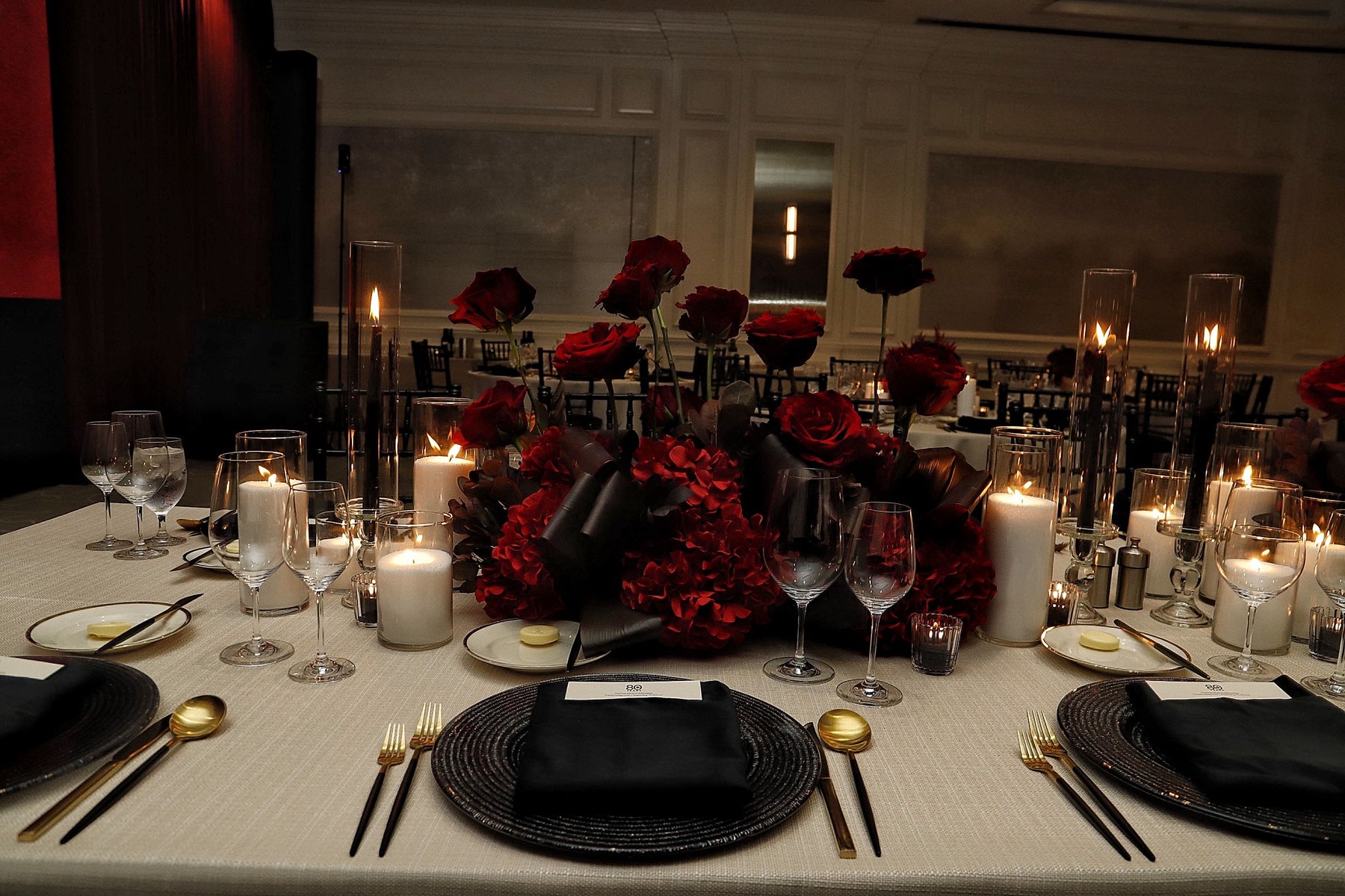 Four Seasons reception table with glass cylinder candlelight, red florals, and black place settings