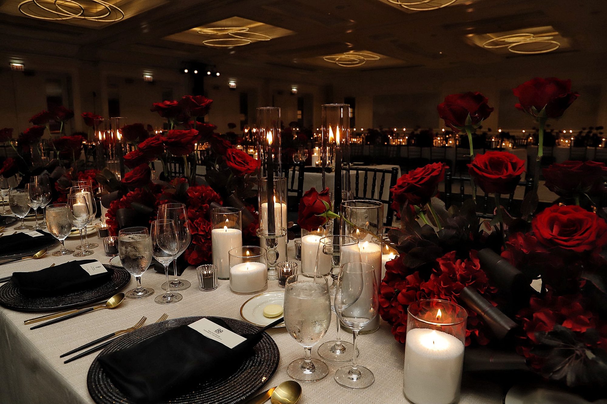 Layered glass candlelight and red roses across a reception table