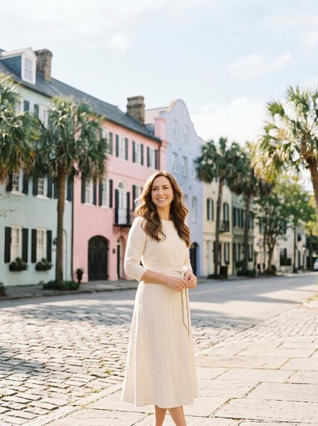 Woman in a cream dress on a Charleston street lined with pastel houses and palm trees