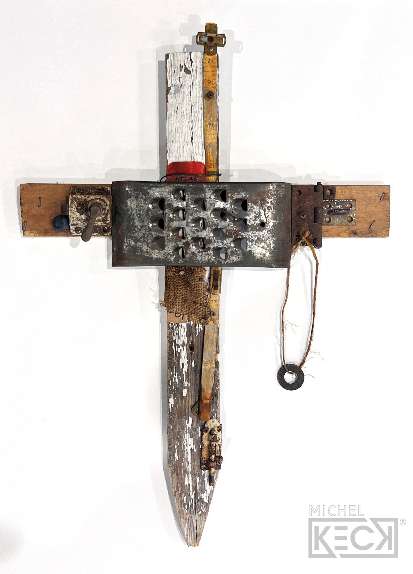 Michel Keck cross assemblage featuring weathered wood pieces in white and natural tones, a rusted metal grate with protrusions, a hanging circular washer tied with string, and various metal and fabric elements arranged vertically and horizontally.