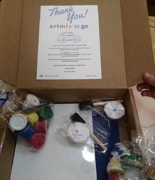 Open cardboard box containing small paint containers in various colors, paintbrushes, and a white canvas board, with a printed thank you note from Michel Keck's artmix to go on the inside lid.