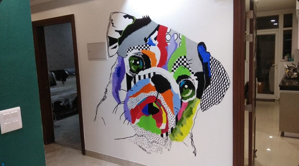 Wall mural by Michel Keck depicting a dog's face with large green eyes, composed of colorful abstract shapes and patterns including checkerboard, stripes, and solid colors, painted on a white wall in a modern interior space.