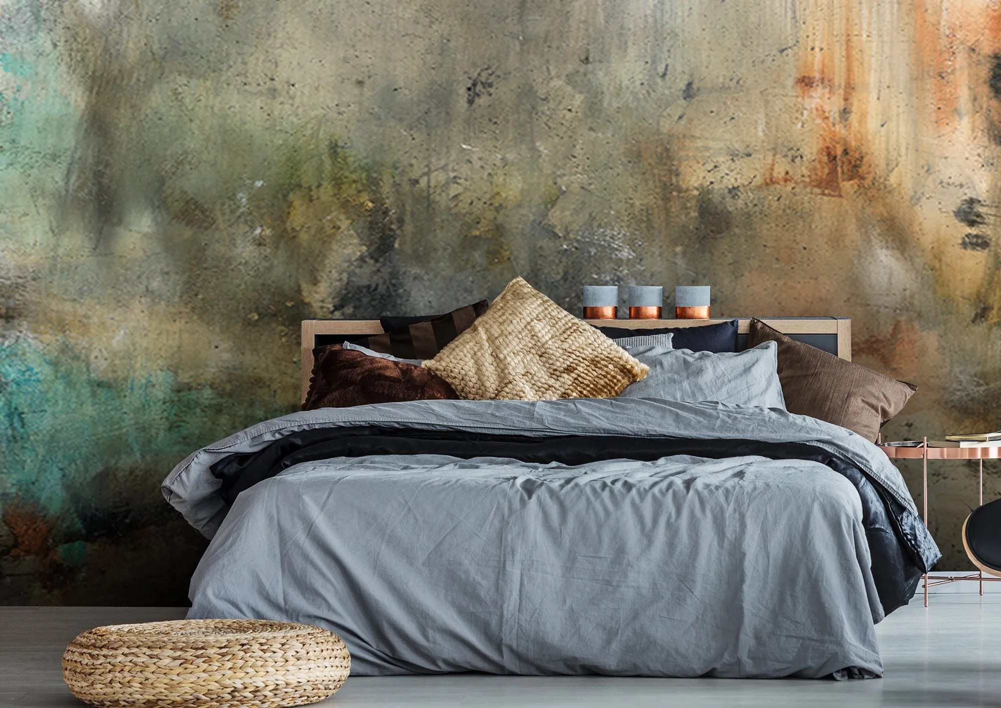 Michel Keck wall mural with textured abstract patterns in muted greens, browns, and rust tones behind a modern bed with gray bedding, assorted pillows, and a woven round ottoman on a light floor.