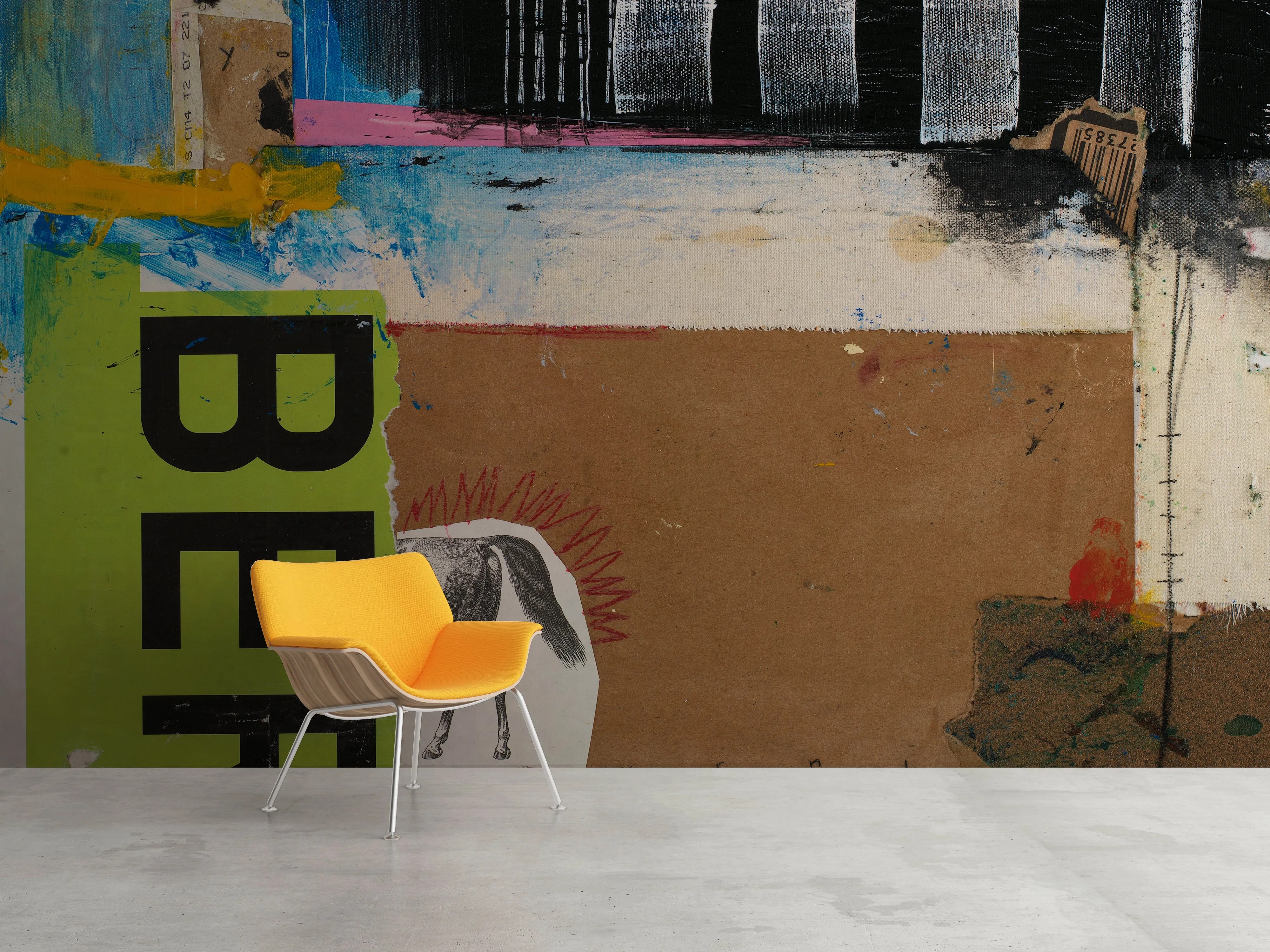 Large removable wall mural by Michel Keck featuring layered abstract shapes and textures in green, brown, black, blue, and white with bold black letters and a partial horse drawing, set behind a modern yellow chair on a smooth concrete floor.