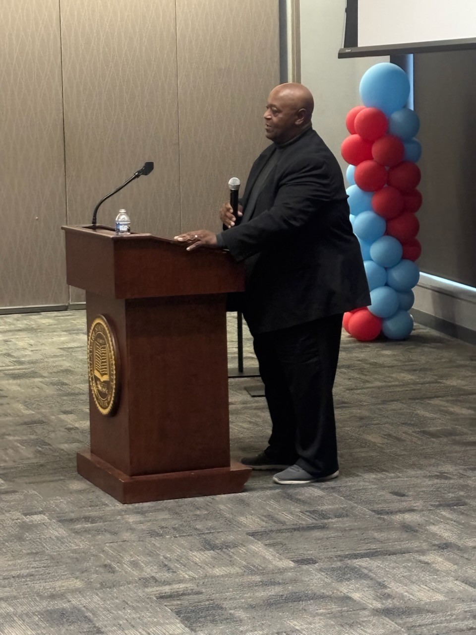 Grandmaster Kemmerlin presenting at a lectern during the Delaware State University Football Legends Homecoming Meet and Greet