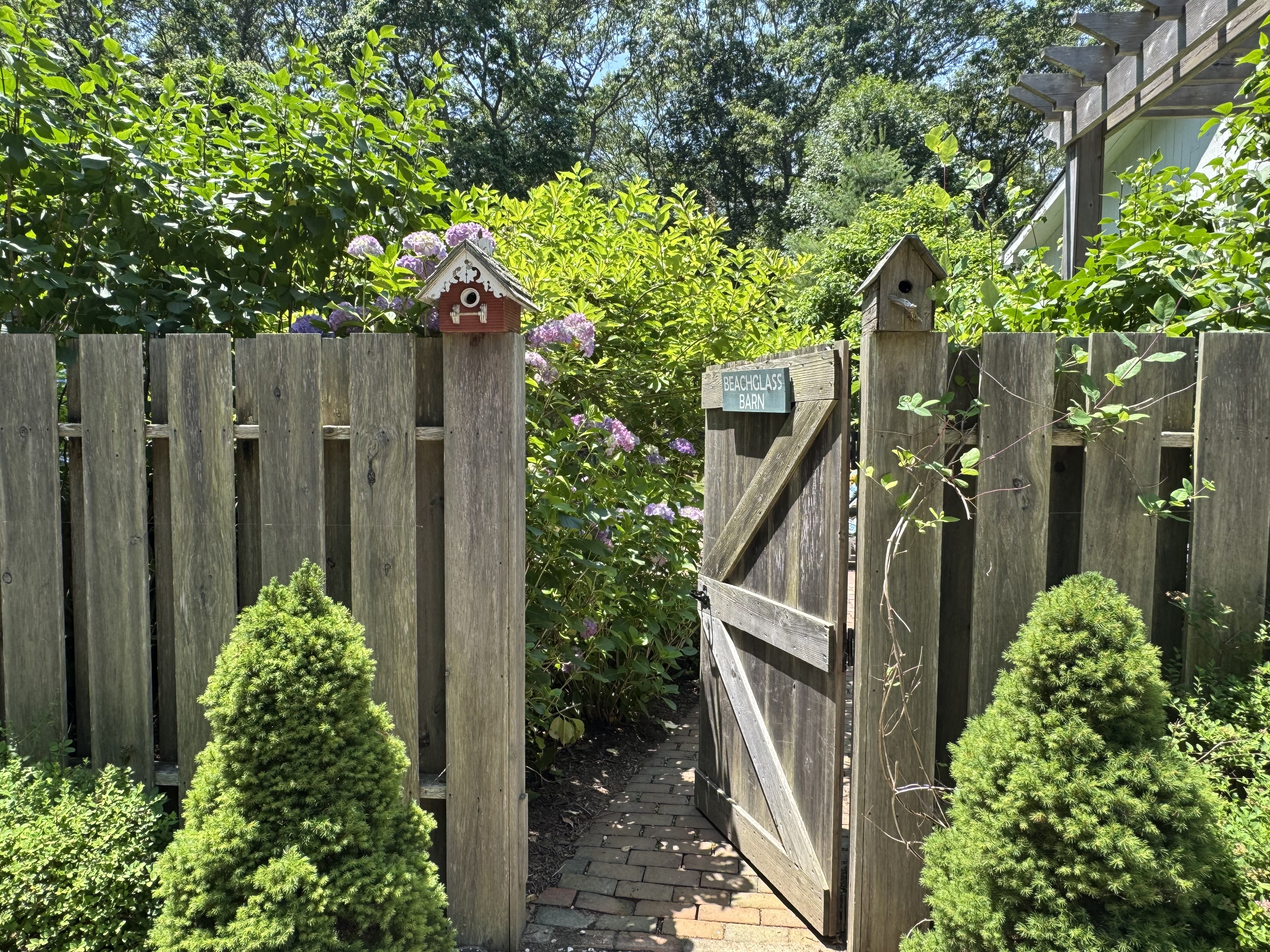Open Beachglass Barn garden gate with hydrangeas and birdhouses