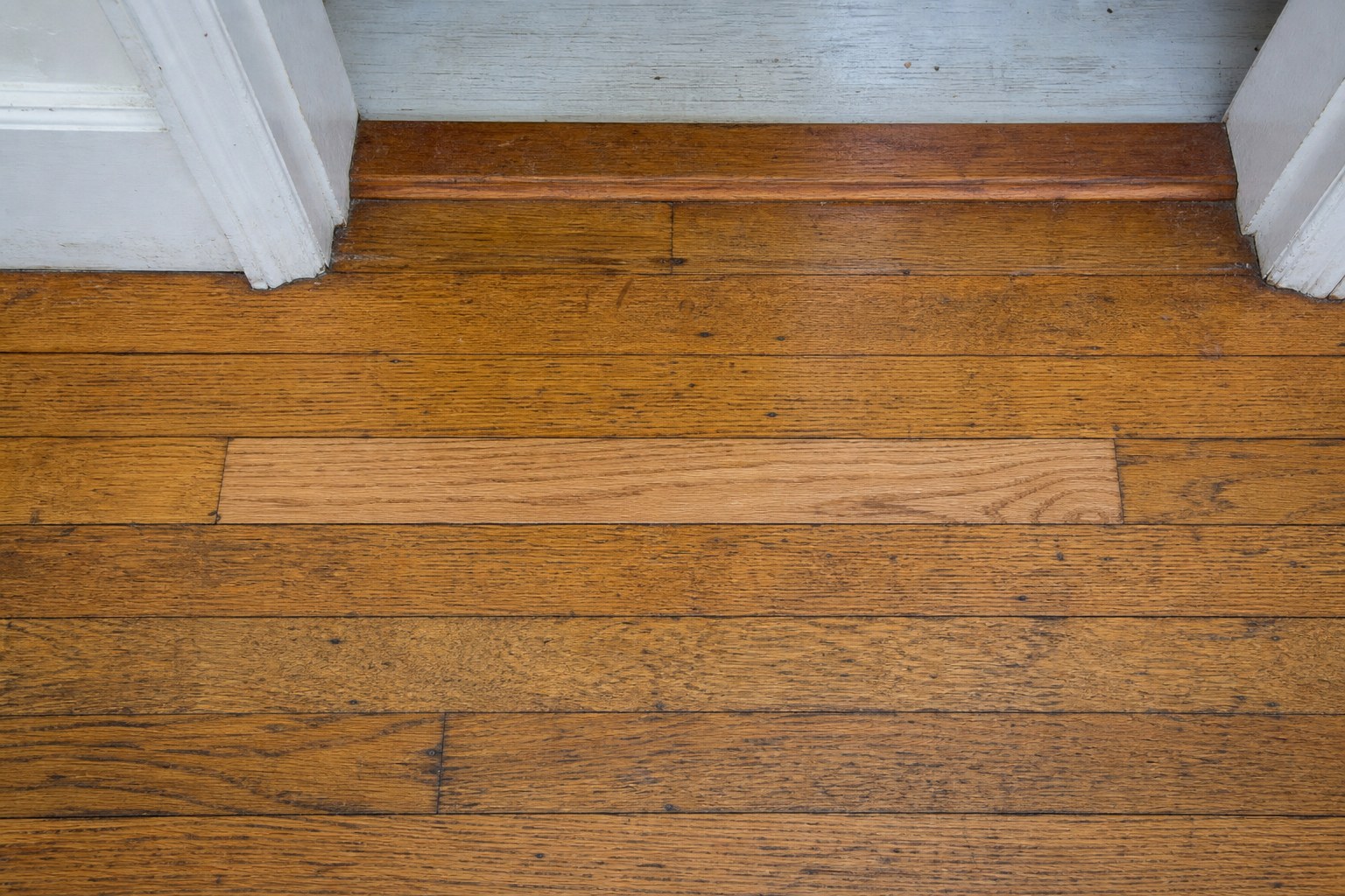 Thoughtful oak board repair integrated into an older hardwood floor at a doorway