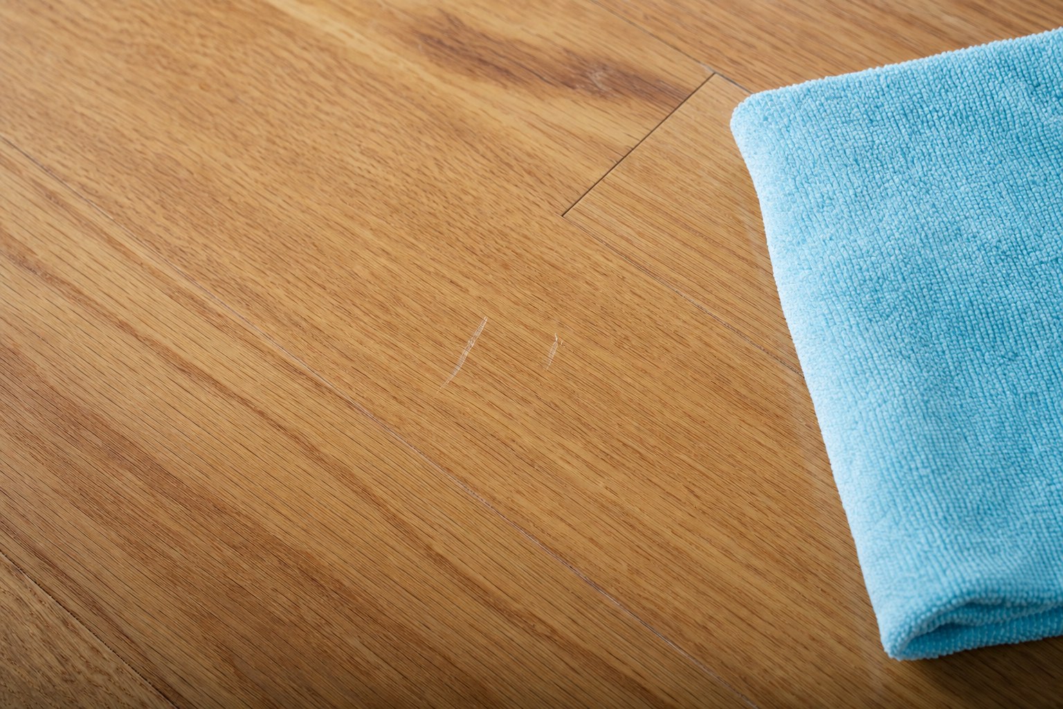 Small surface scuffs beside a microfiber cloth on a natural oak hardwood floor