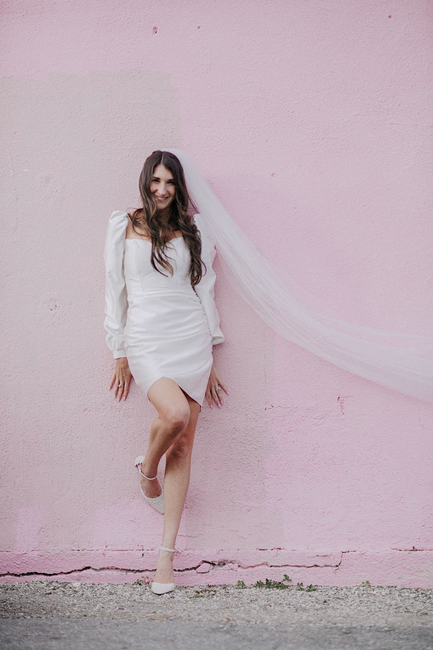 Bride in a short wedding dress and veil against a pink wall