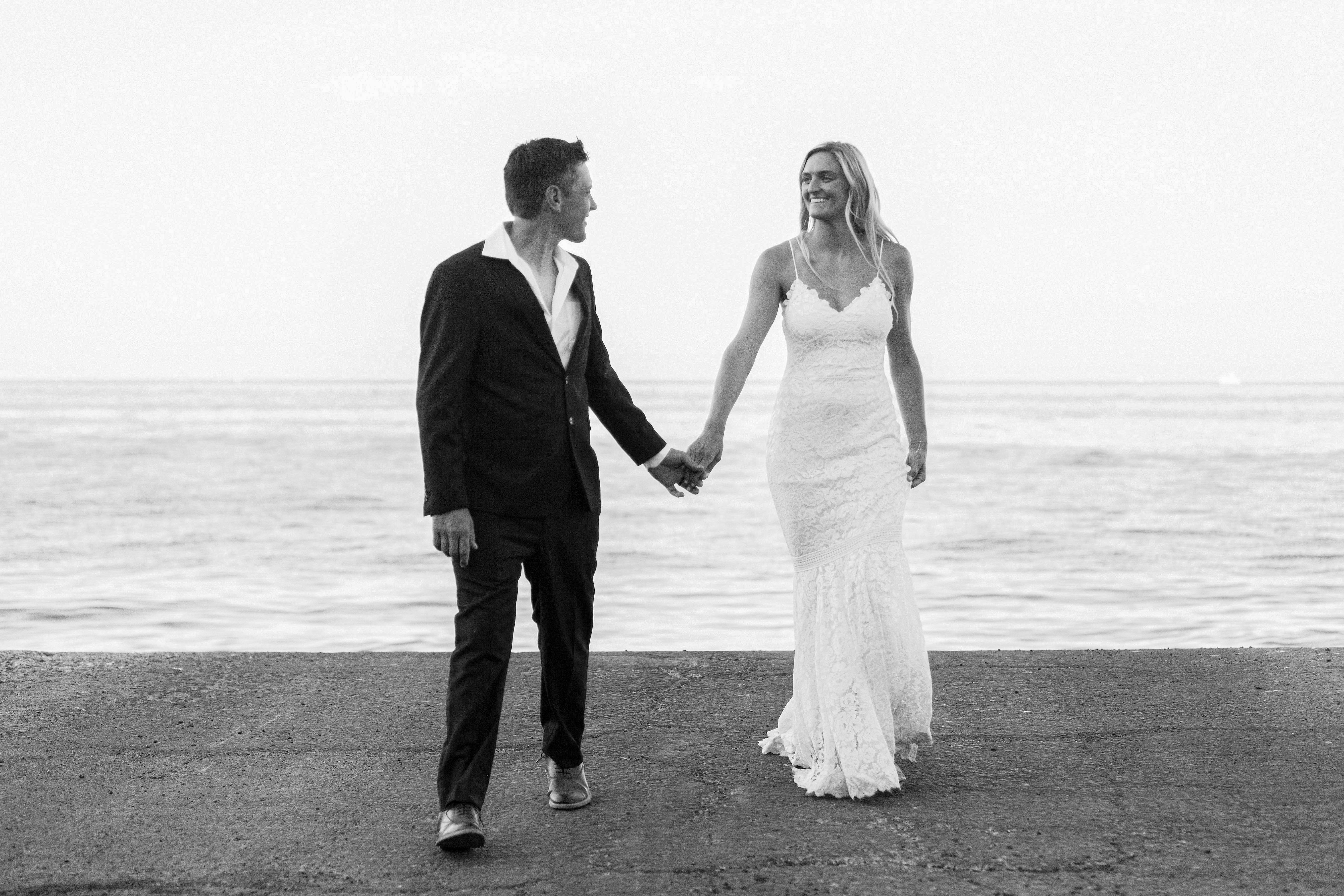 Newlyweds walking hand in hand beside the ocean