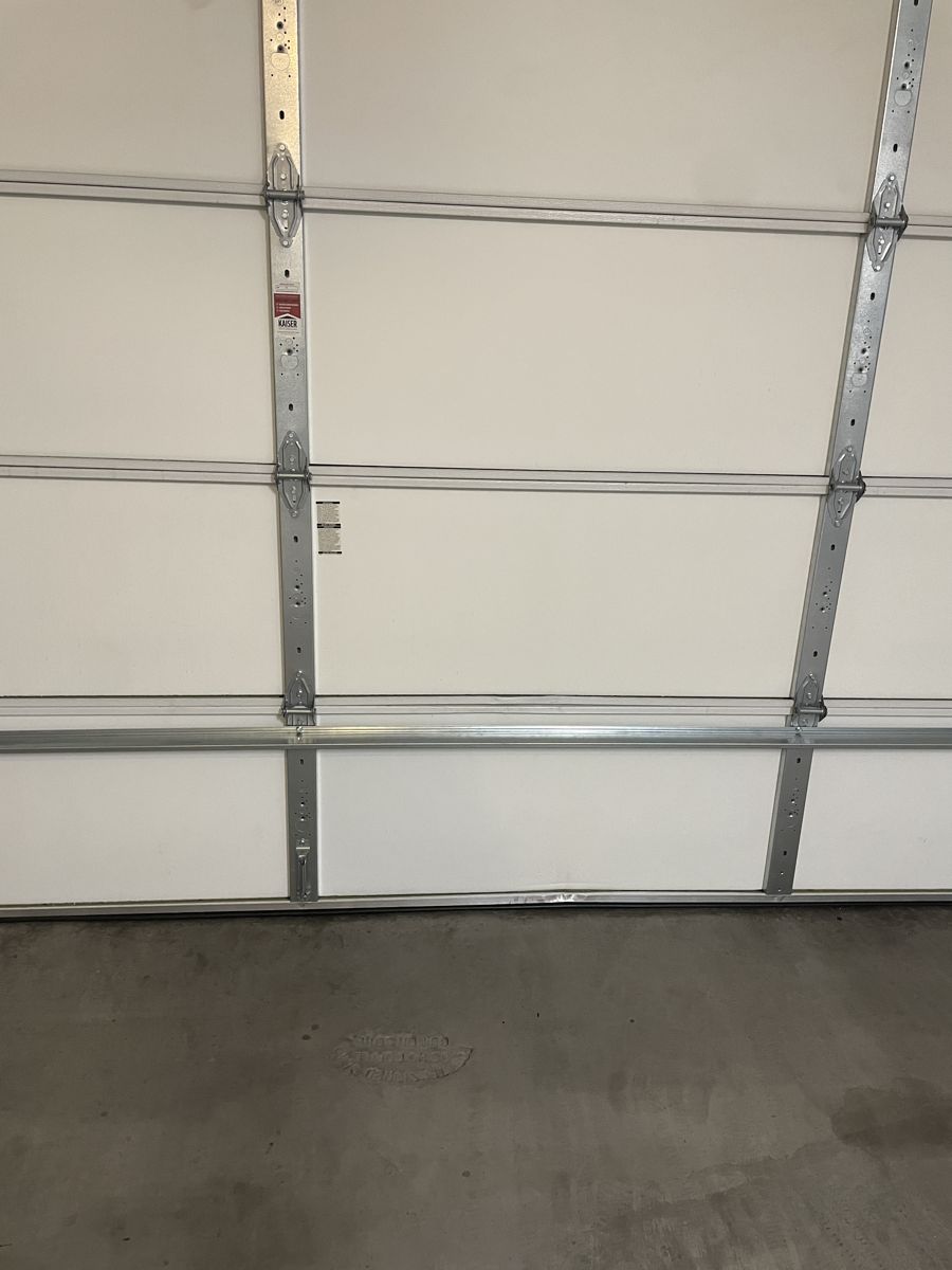 Straightened bottom garage door panel with a reinforcing strut added
