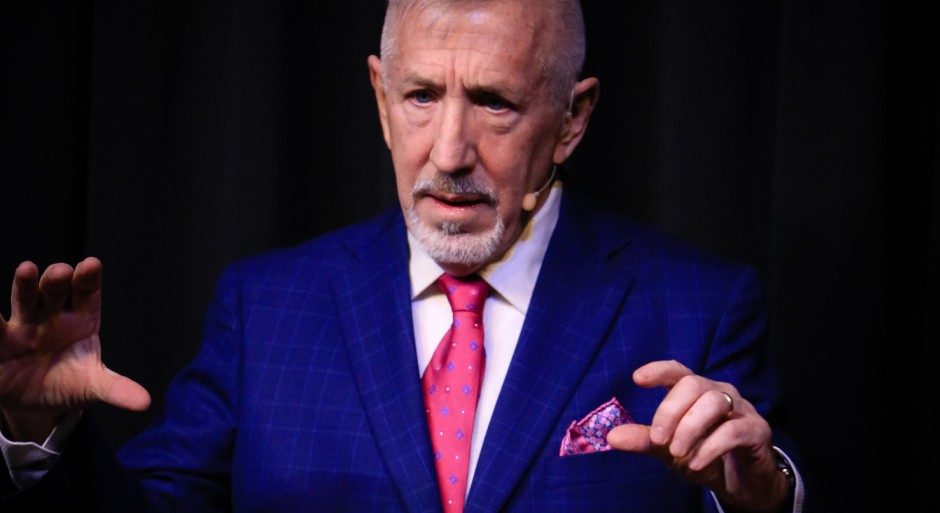 boB speaking onstage in a blue suit with a pink tie