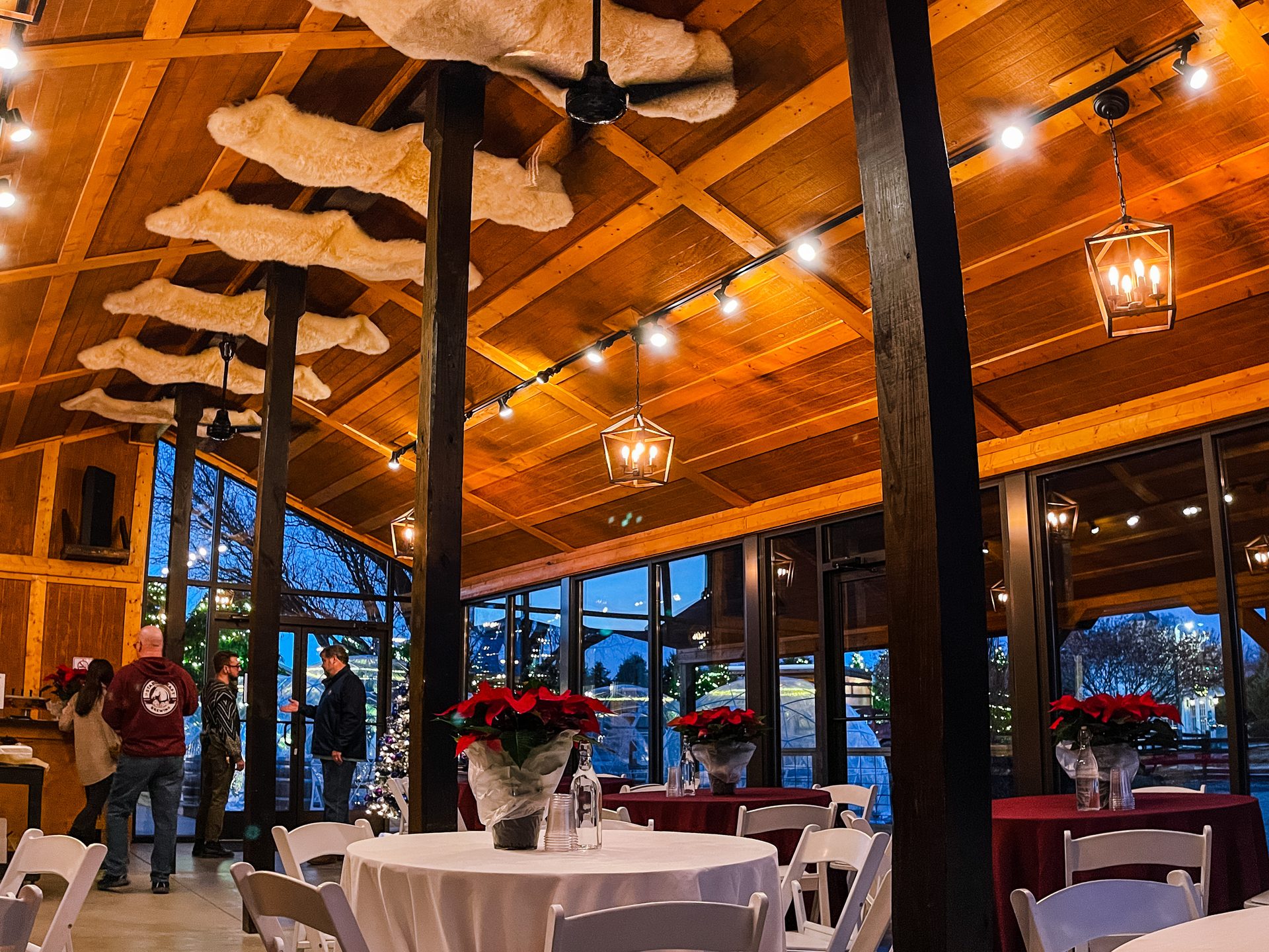 Stable Craft Brewing event space decorated for the holidays with poinsettias, lanterns, and tables ready for guests