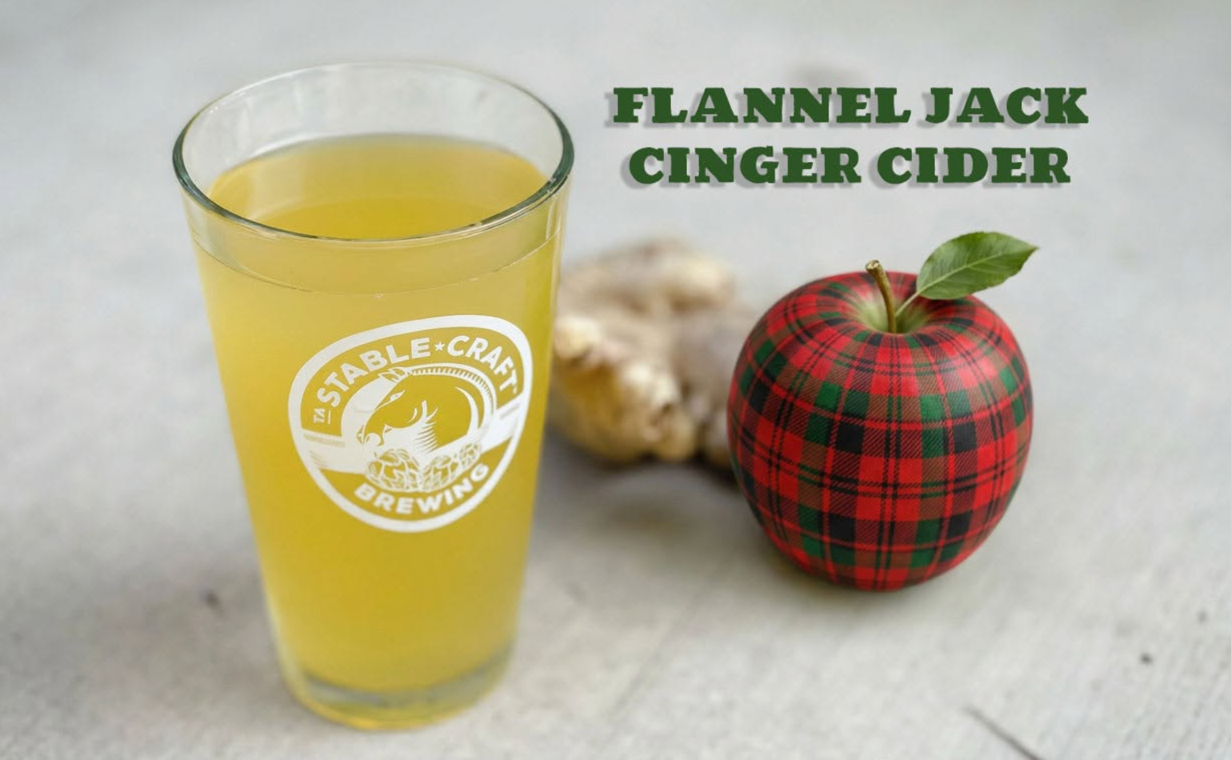 Flannel Jack Ginger Cider in a Stable Craft glass beside a plaid apple