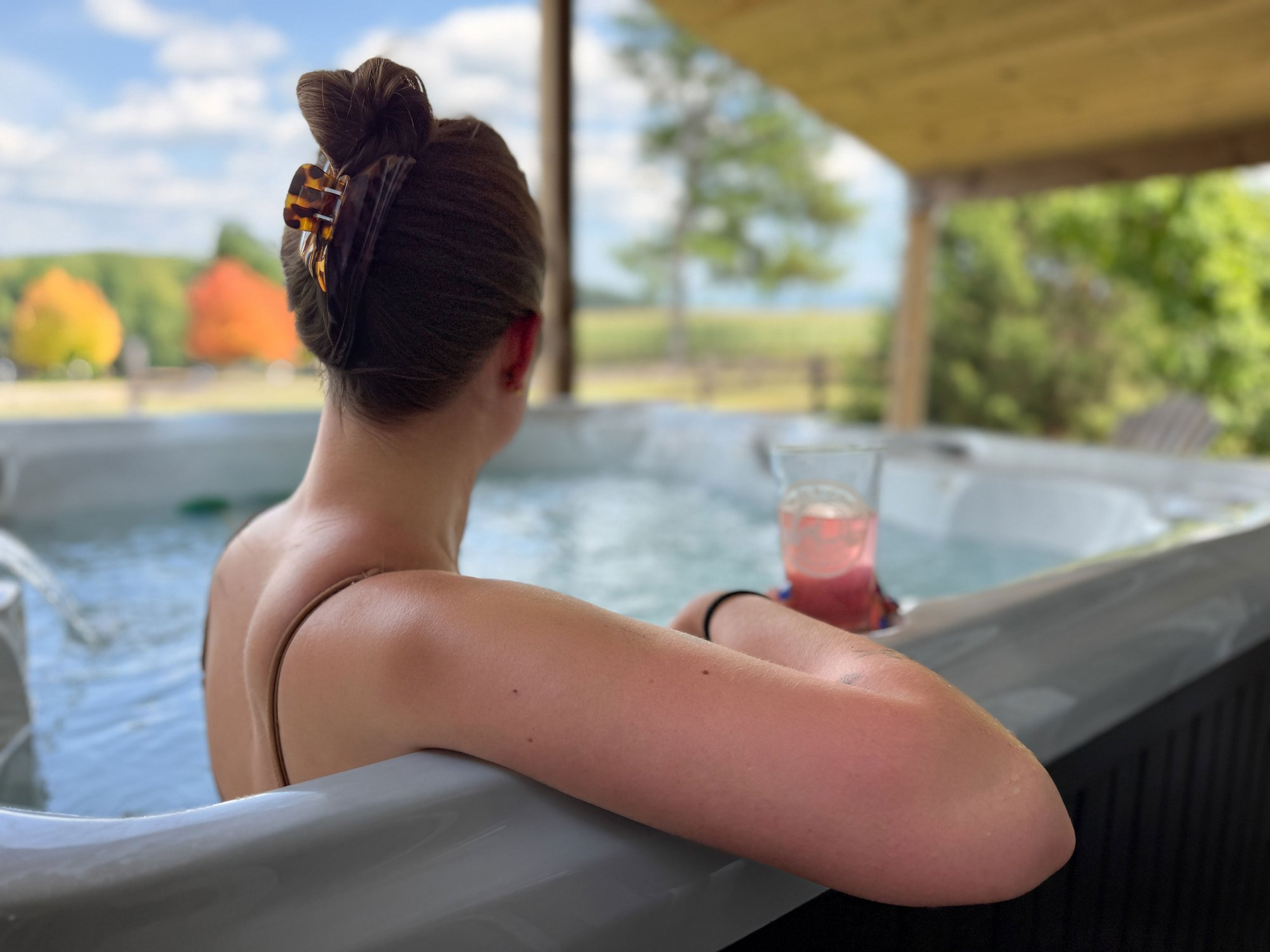 Guest relaxing in a private hot tub with fall colors beyond the porch