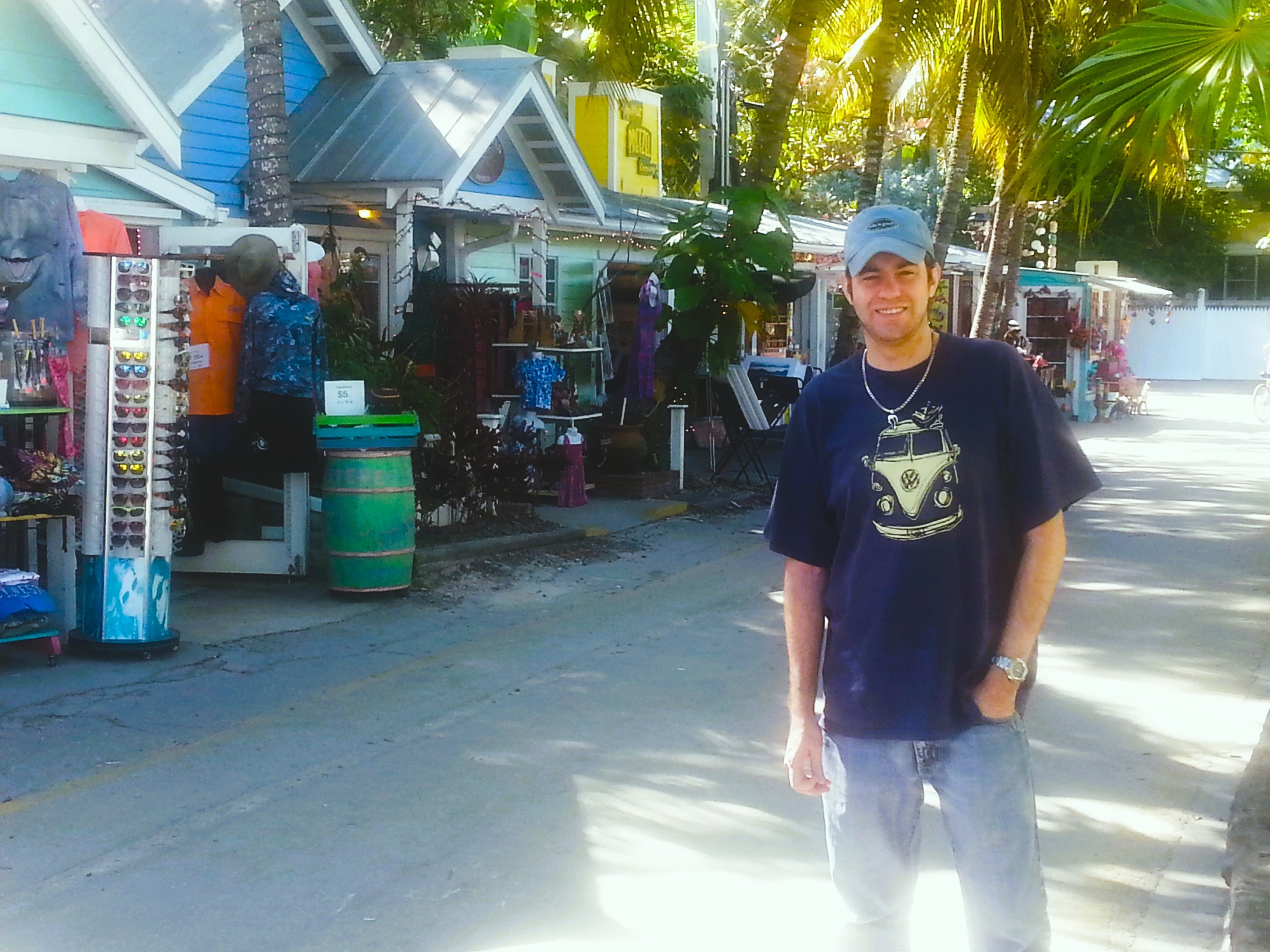 A shopper wearing a Volkswagen bus T-shirt among colorful shops and palm trees in Key West