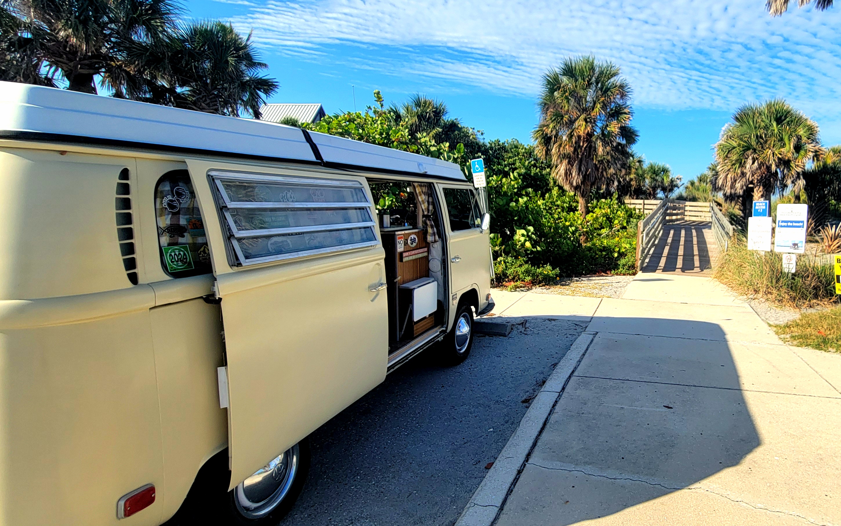 A vintage Volkswagen camper parked beside a beach access path
