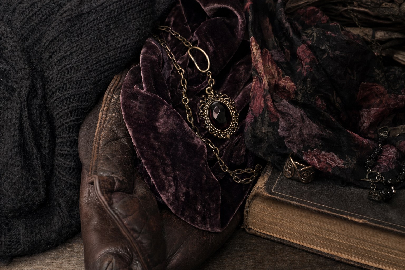 Black knit, plum velvet, leather, floral fabric, brass jewelry, and a vintage book