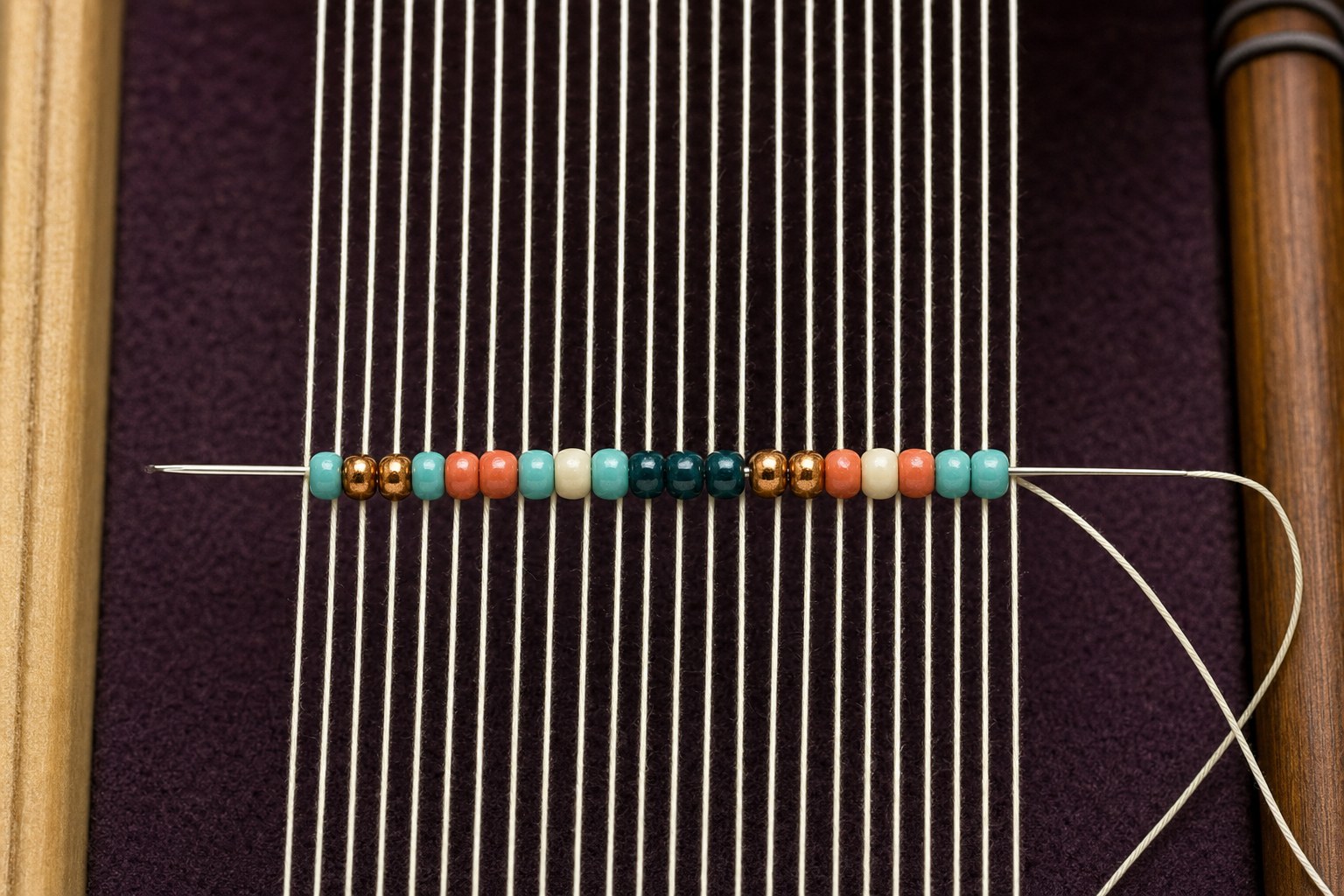 A beading needle passing through a row of colored seed beads on a loom