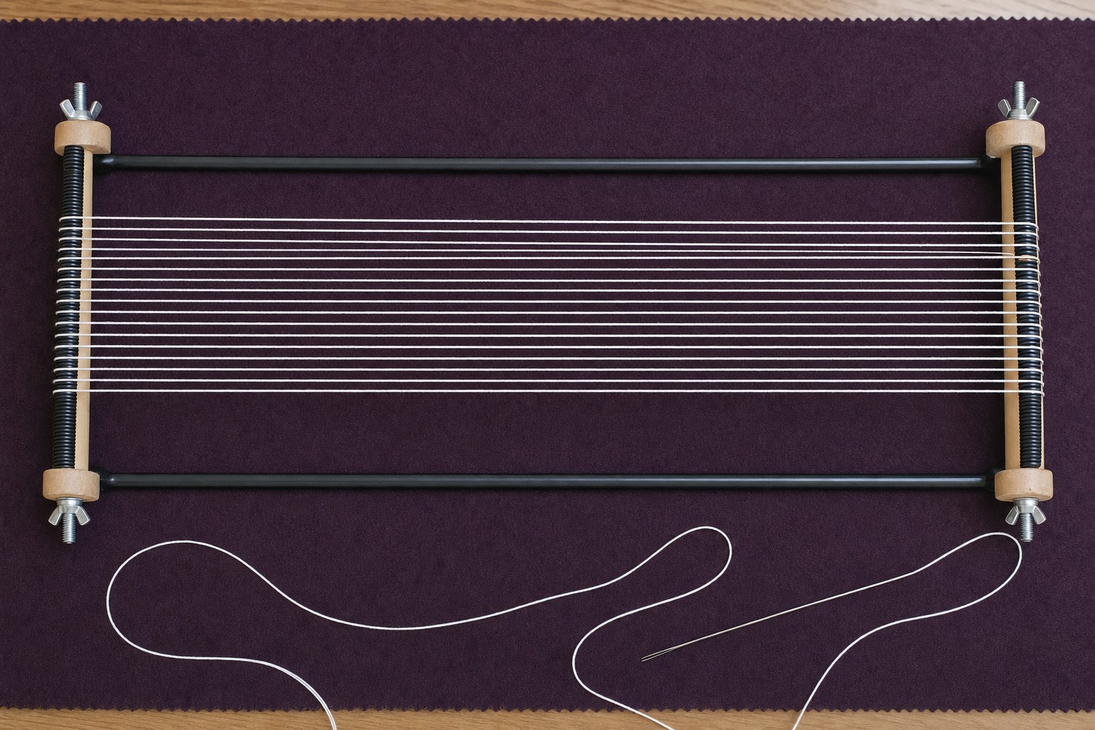A small bead loom with evenly spaced white warp threads before weaving begins