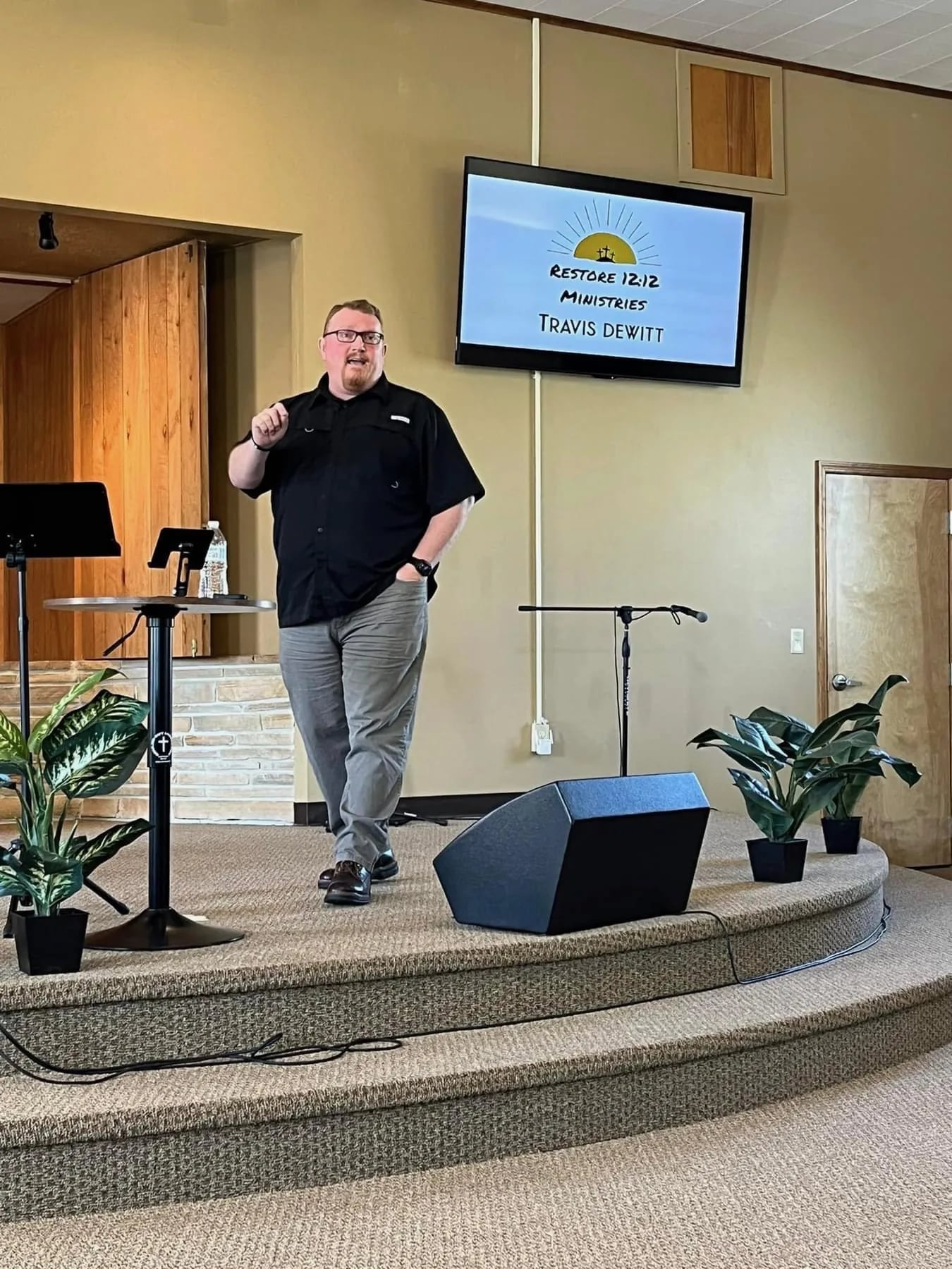 Travis DeWitt speaking at a podium in a community gathering space.