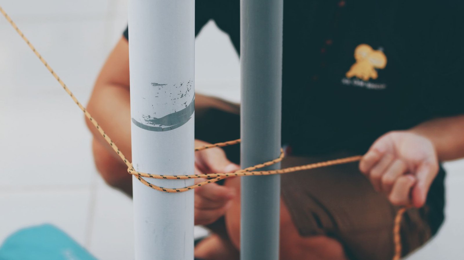 Hands carefully working a rope knot around two supports.