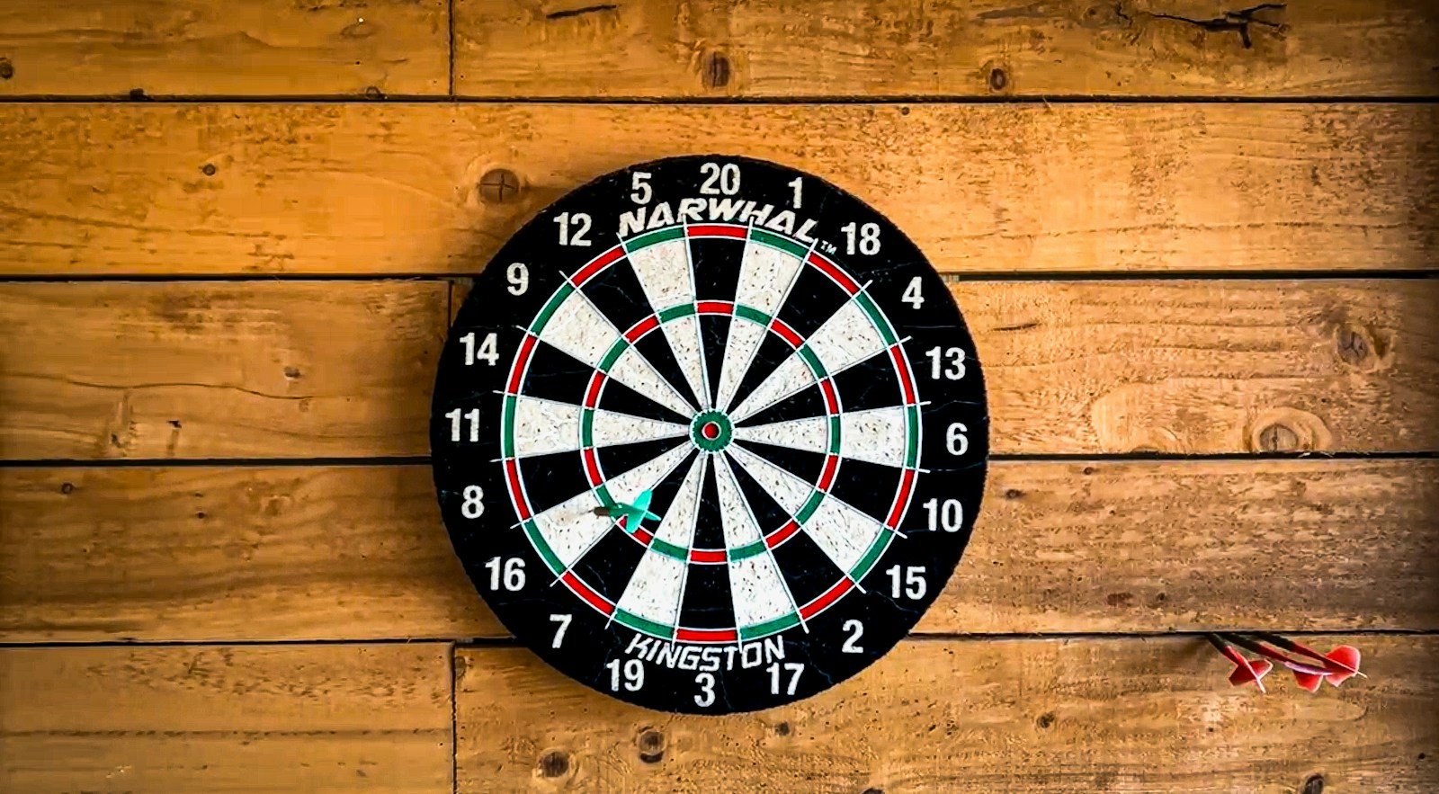 A dartboard mounted on a wooden wall with darts beside it.