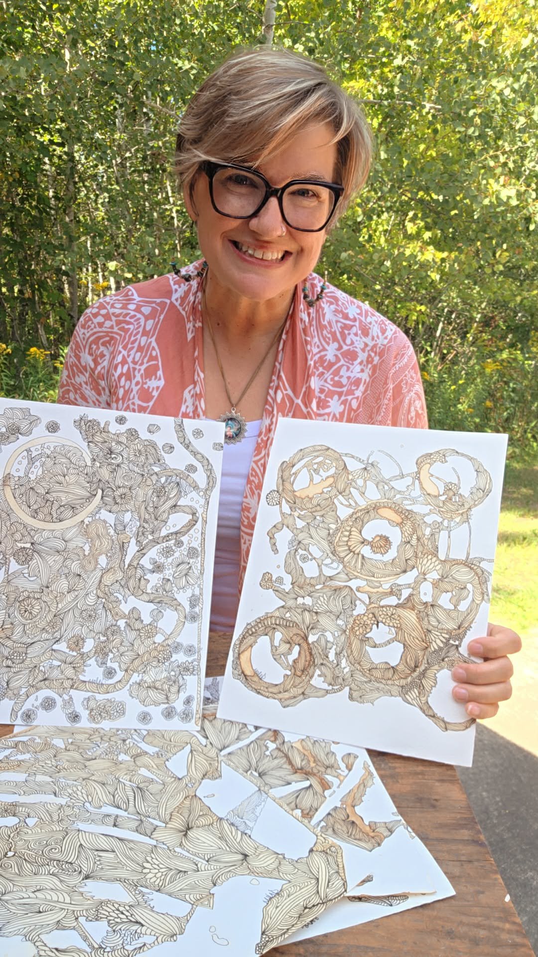 Jennifer Narr outdoors, holding two intricate drawings