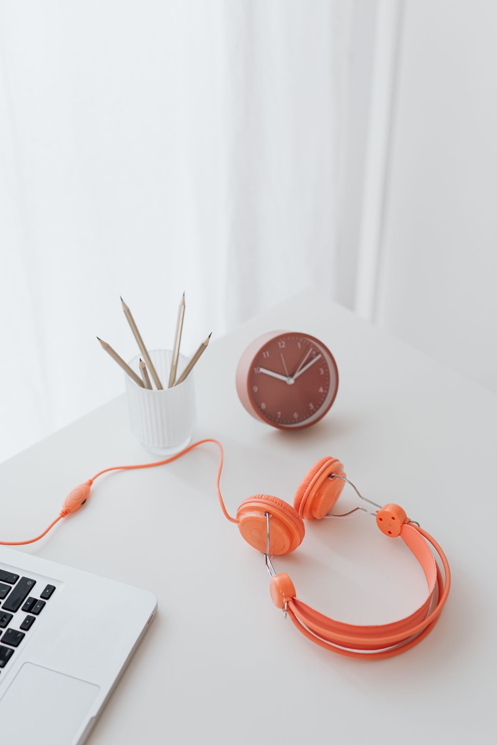 A bright desk with headphones, a notebook, and a clock