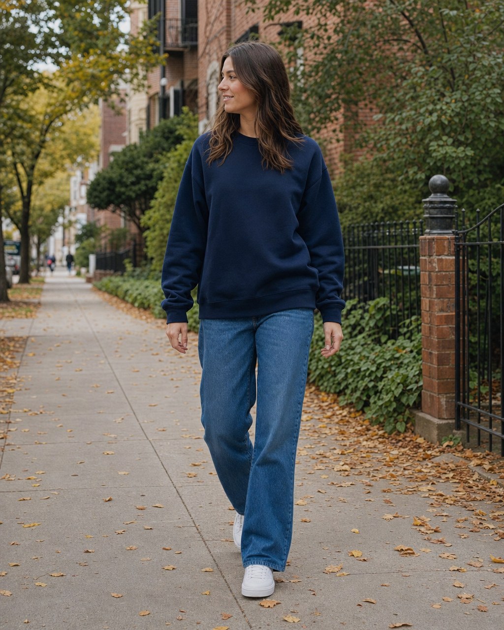 Woman wearing a navy crewneck sweatshirt and blue jeans on a leafy city sidewalk