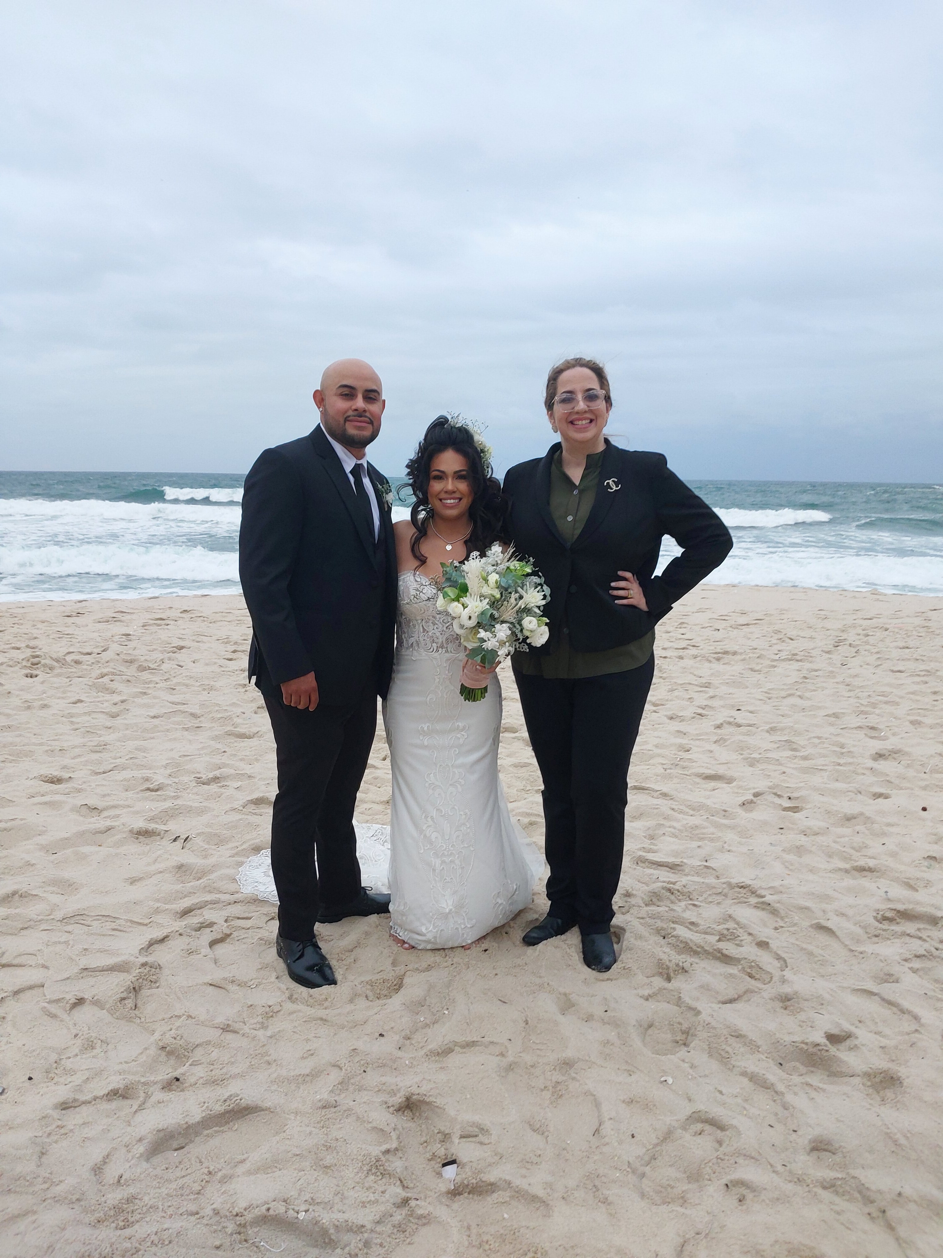 A newly married couple with their officiant on a beach