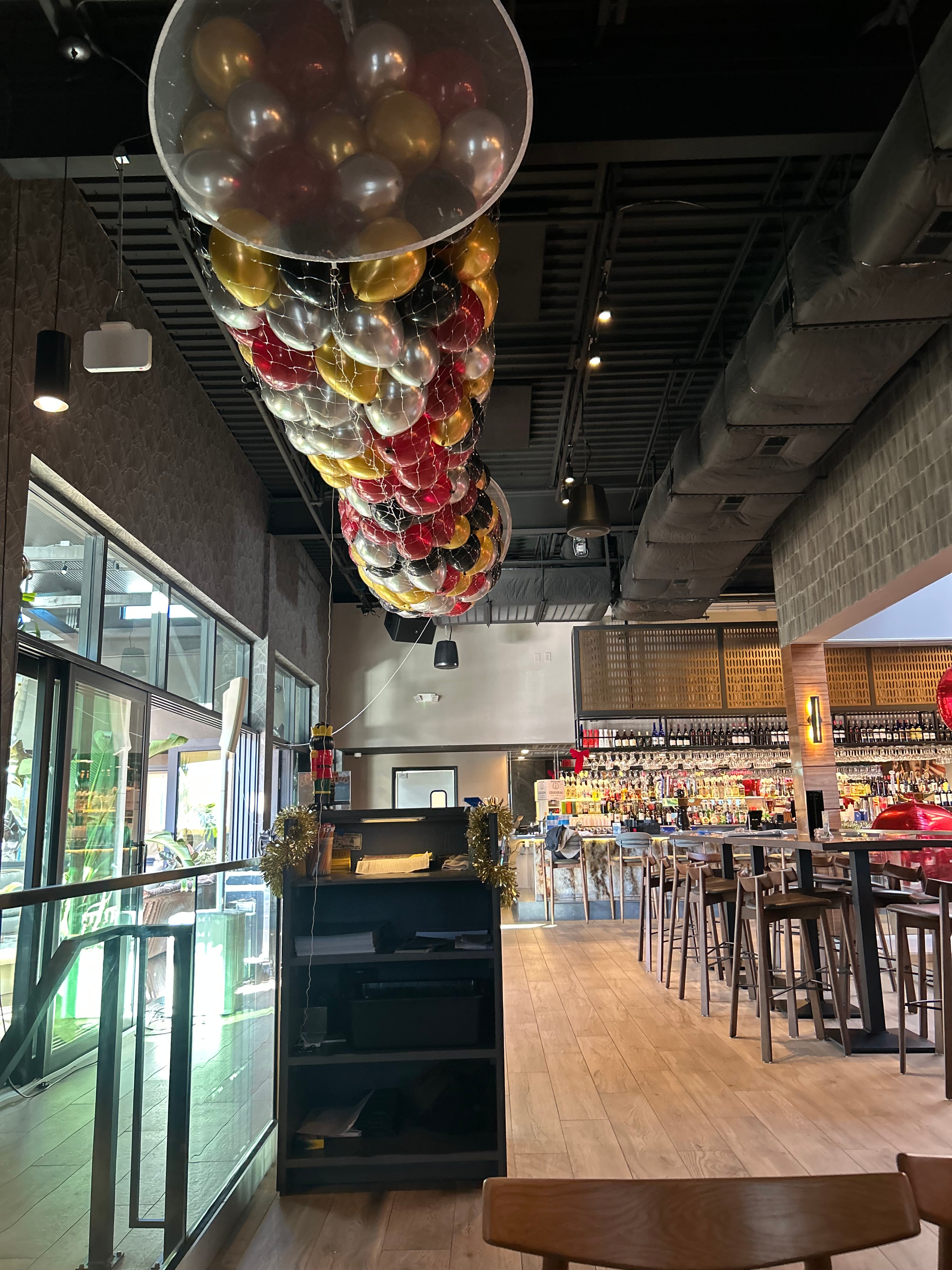 Red, gold, silver, and black balloons held in a ceiling-mounted drop net above an event space