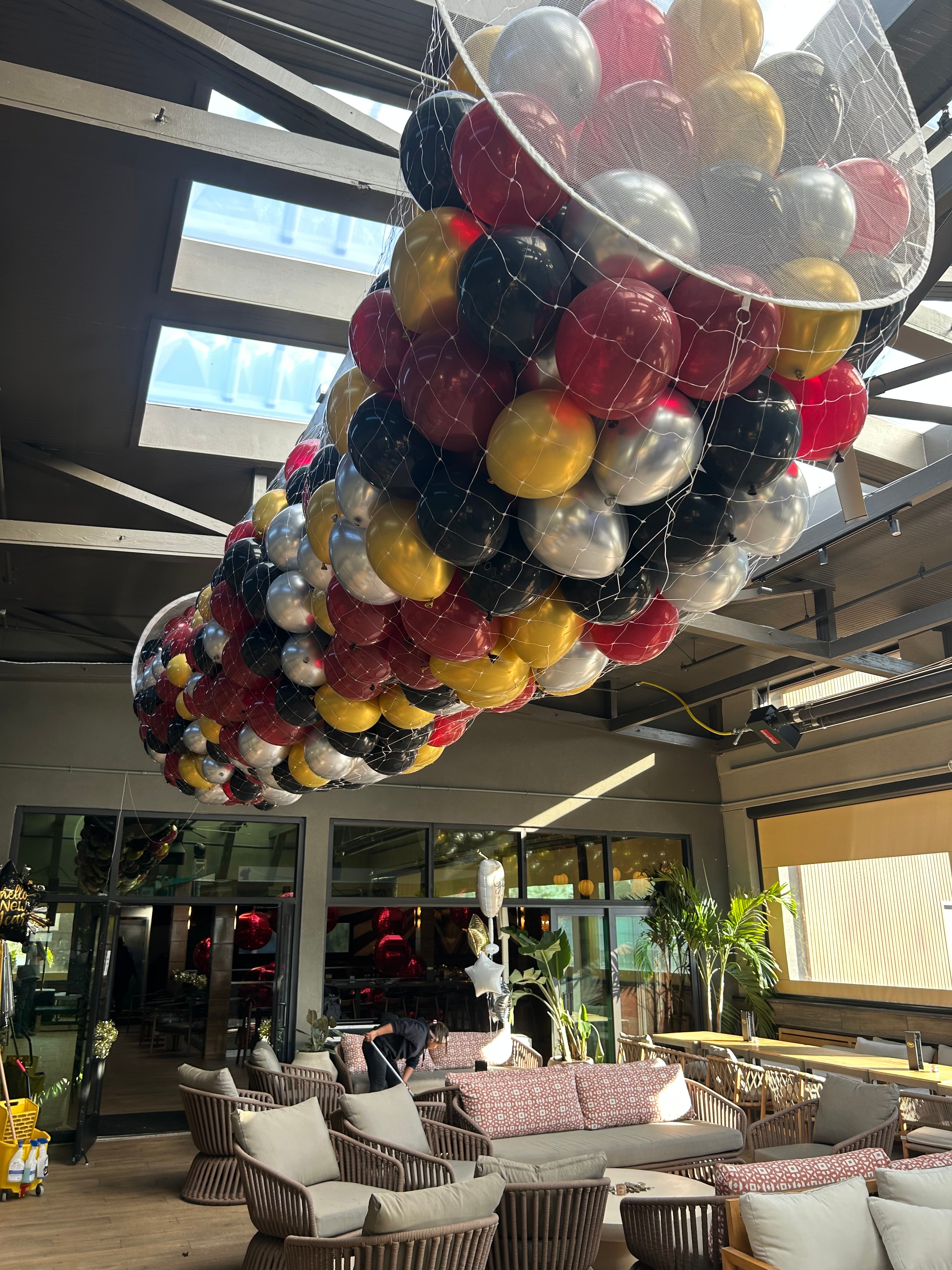 Ceiling-mounted balloon drop filled with red, gold, black, and silver balloons