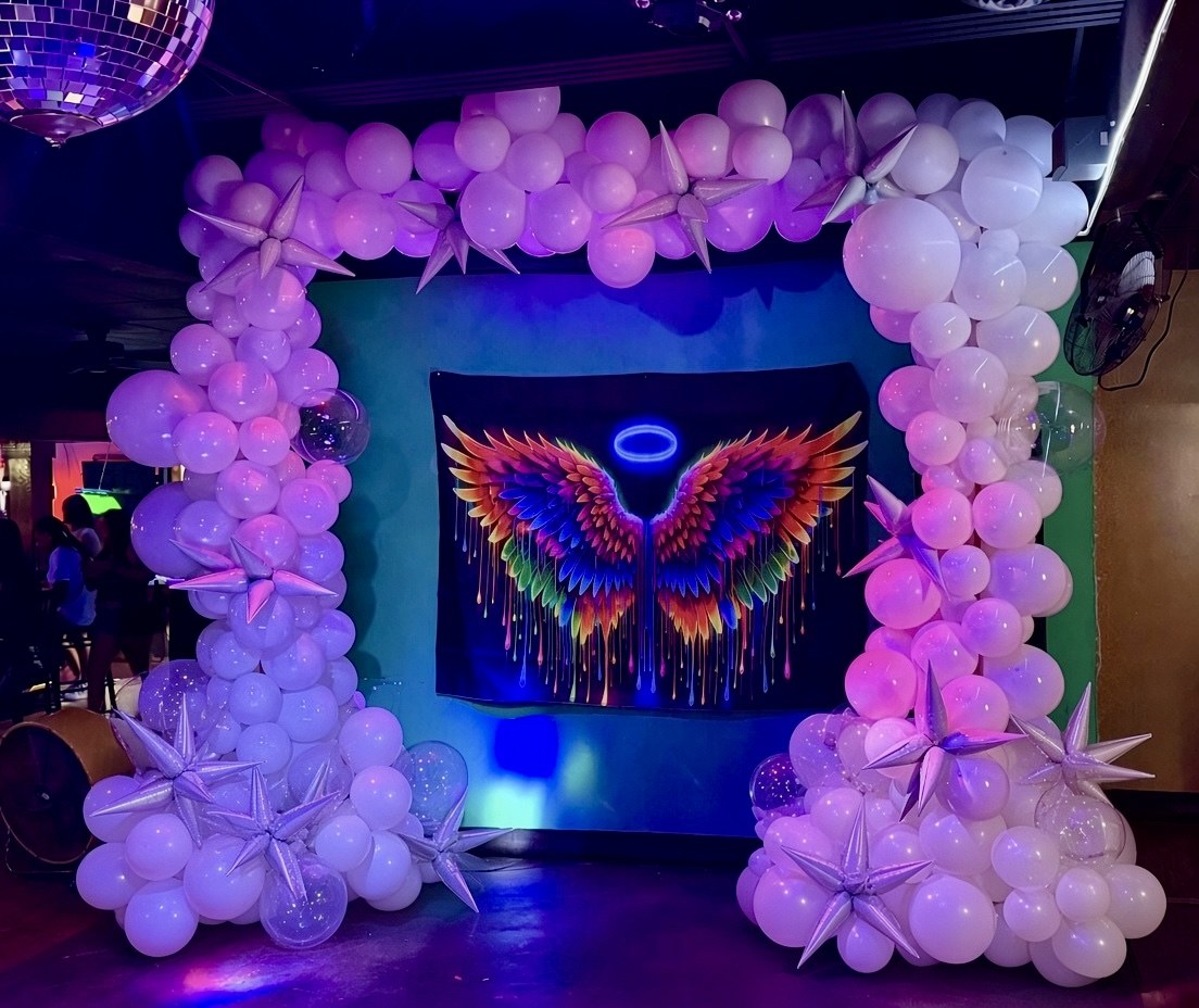 Lavender balloon arch with star accents framing a colorful angel-wing photo backdrop