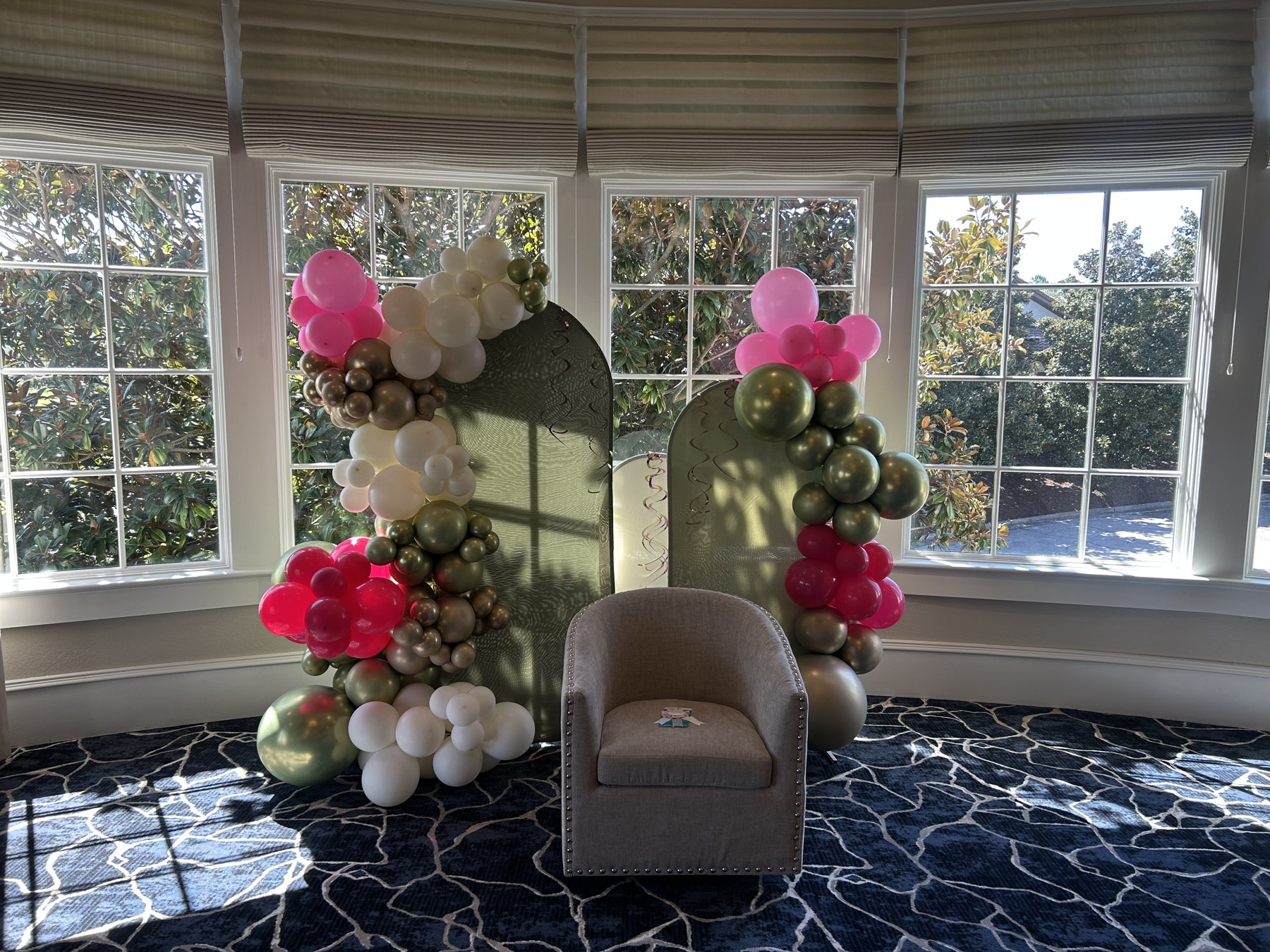 Pink, white, and sage balloon garlands framing a chair and backdrop