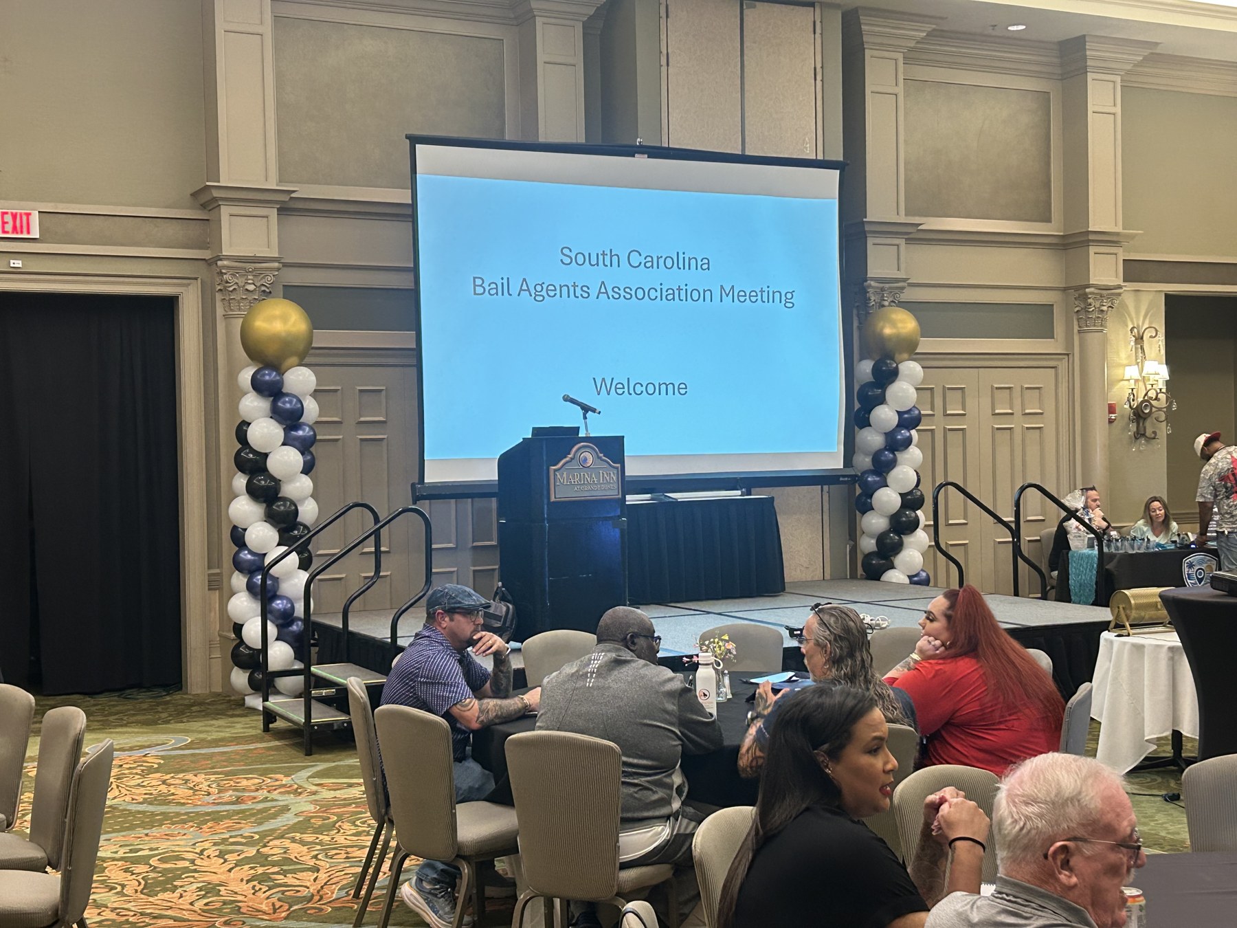 White and gold balloon columns beside a presentation screen at a corporate gathering
