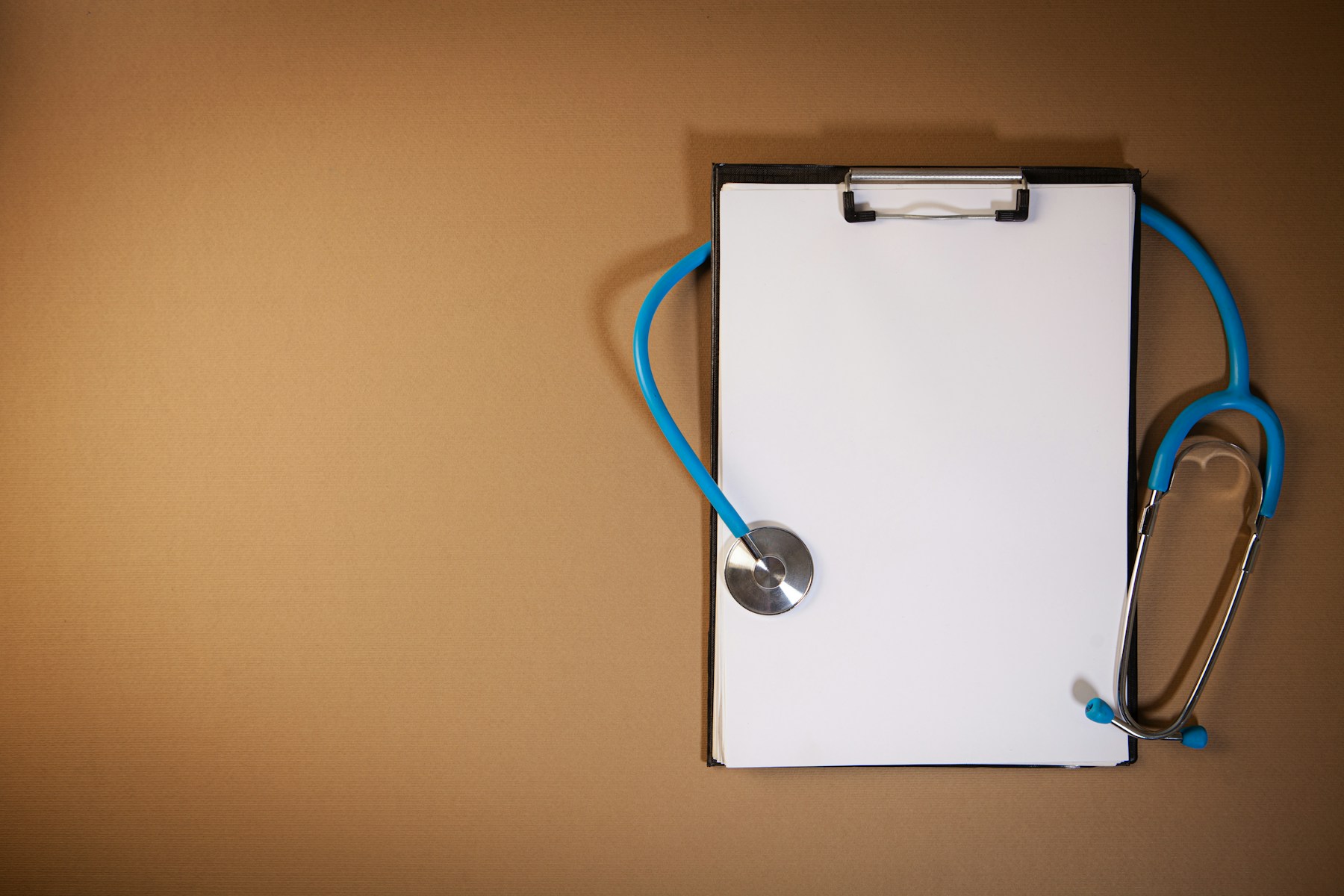 Blue stethoscope arranged on a clipboard against a warm brown background