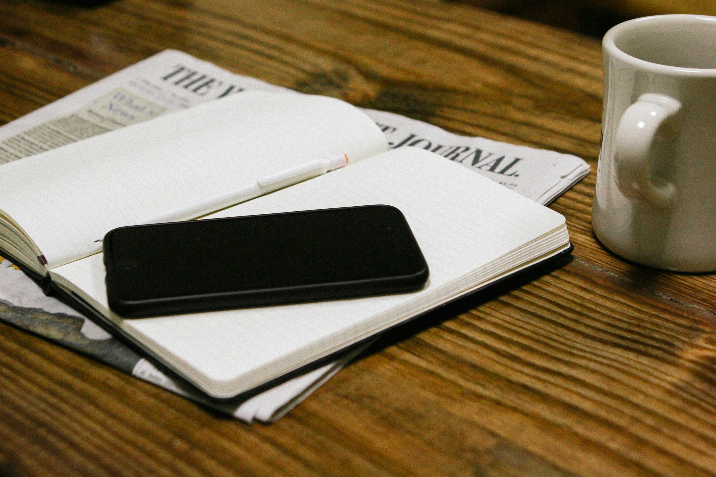 A phone, notebook, and coffee mug on a table
