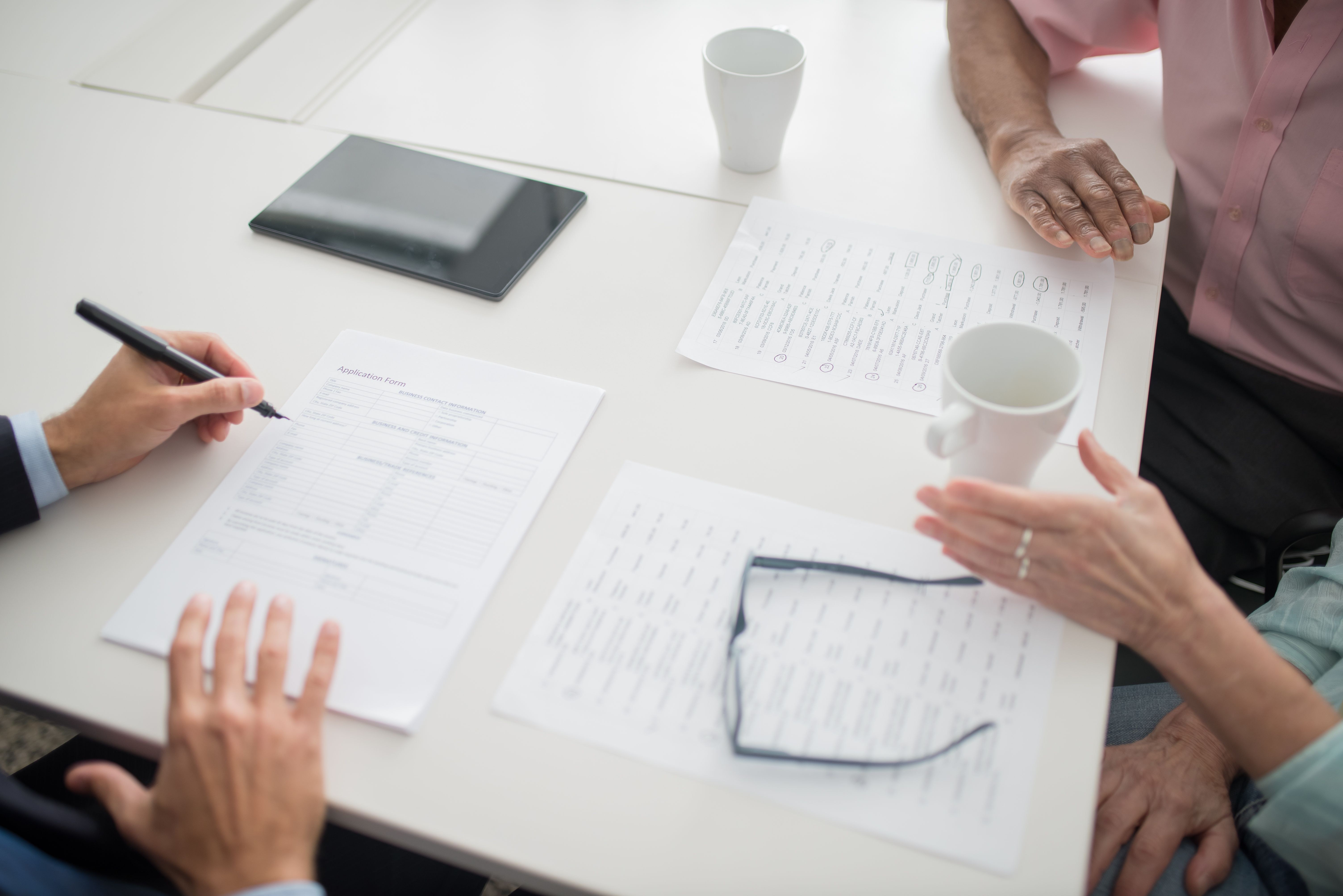 Hands reviewing financial documents with coffee and a tablet