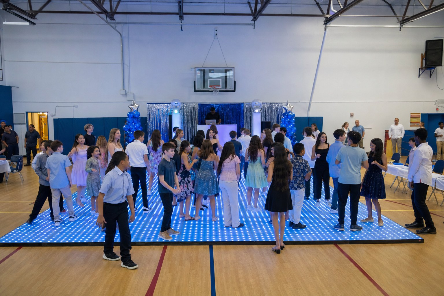Middle school students gathering on a blue LED dance floor at a school gym dance