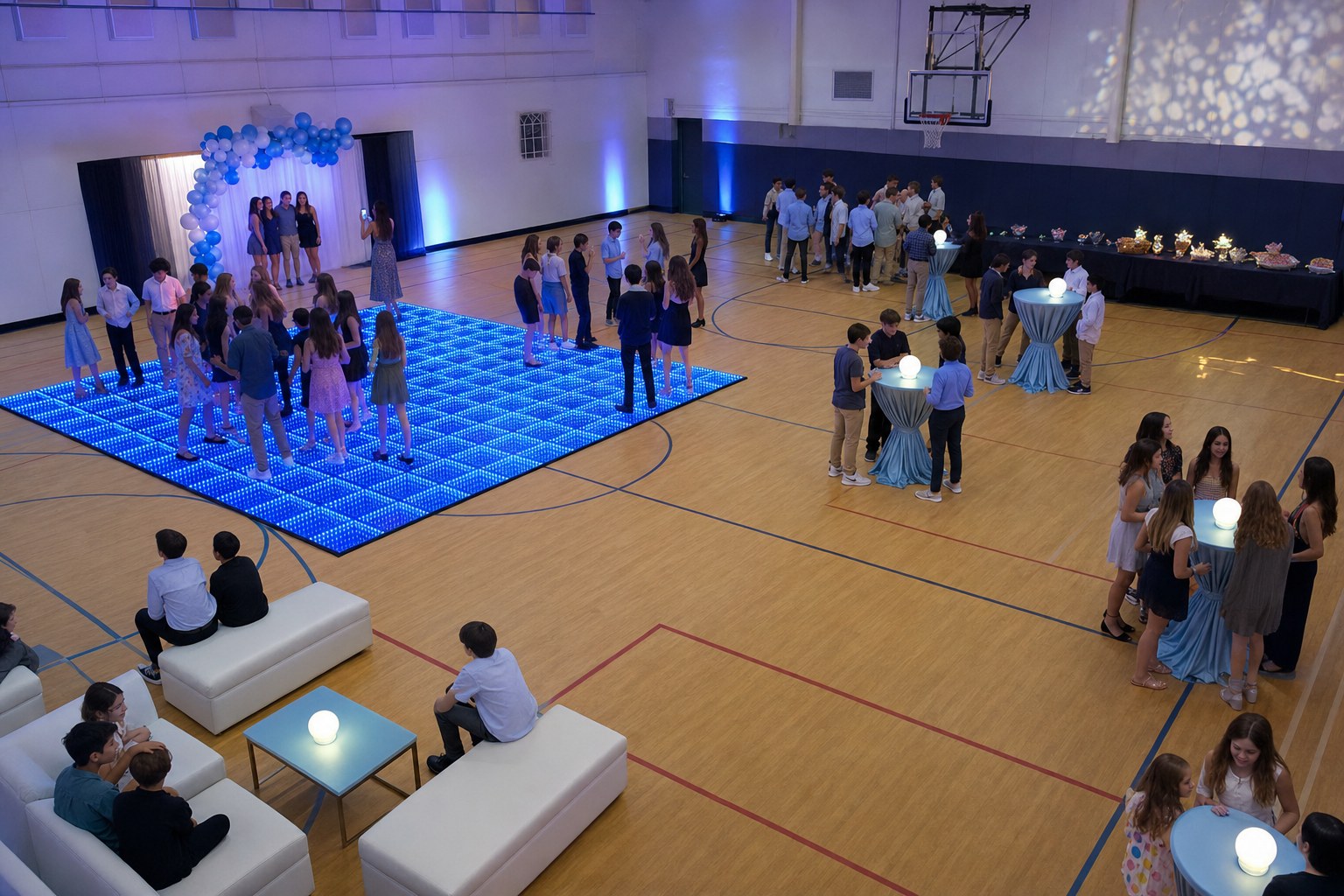 A middle school gym dance with a blue LED floor, photo backdrop, social tables, refreshments, and clear walking paths