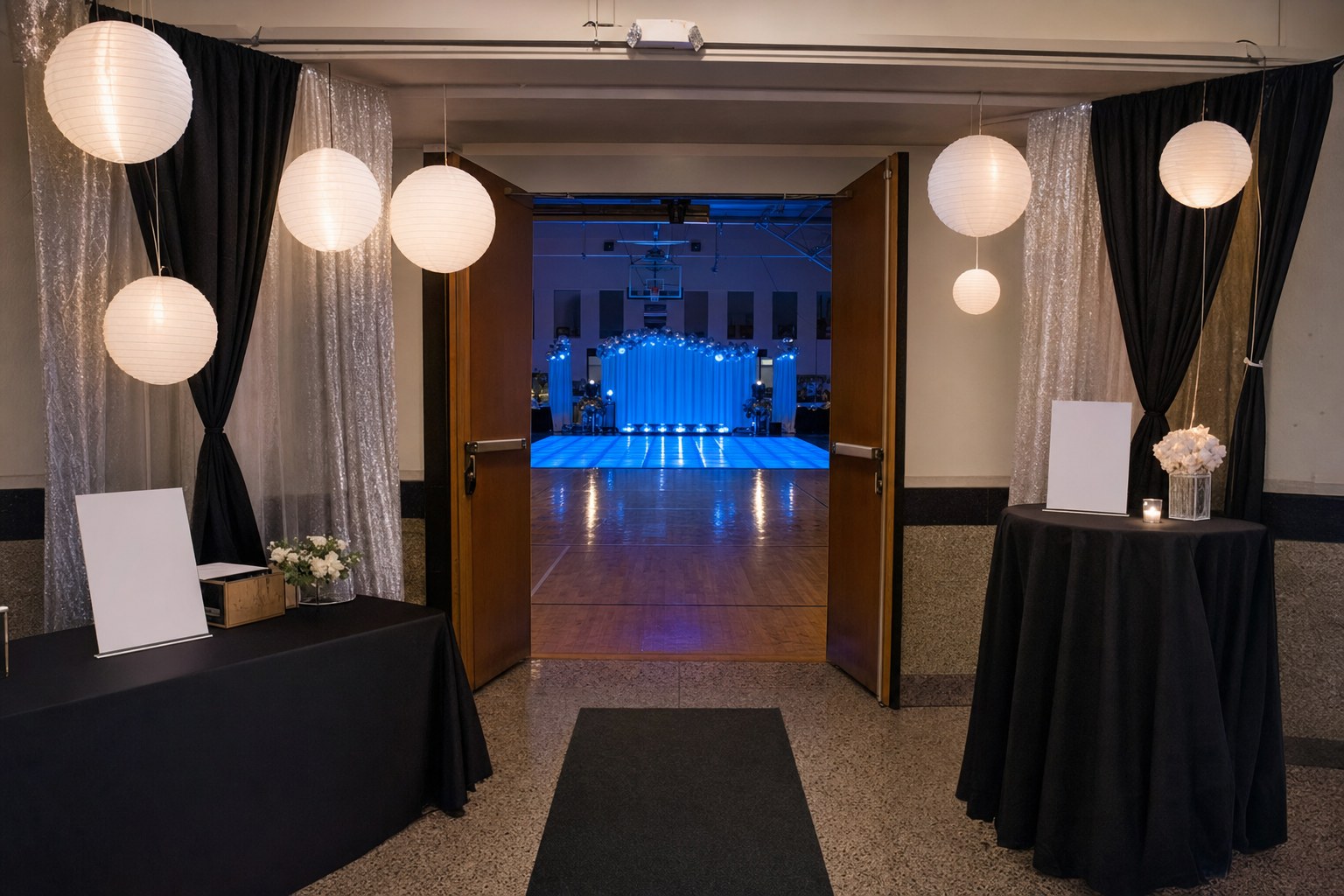 A school gym entrance with paper lanterns, fabric drape, check-in tables, and a view of a blue LED dance floor