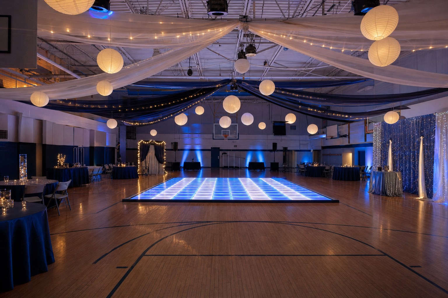 A school gym decorated with lanterns, drape, blue lighting, and an LED dance floor