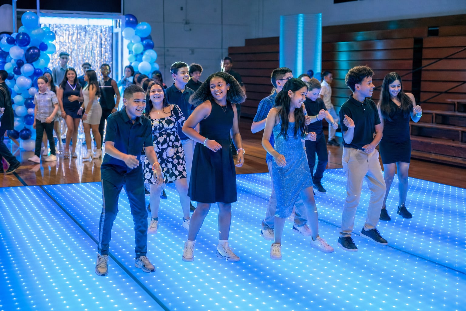 Students joining a group dance on a bright blue LED floor in a school gym