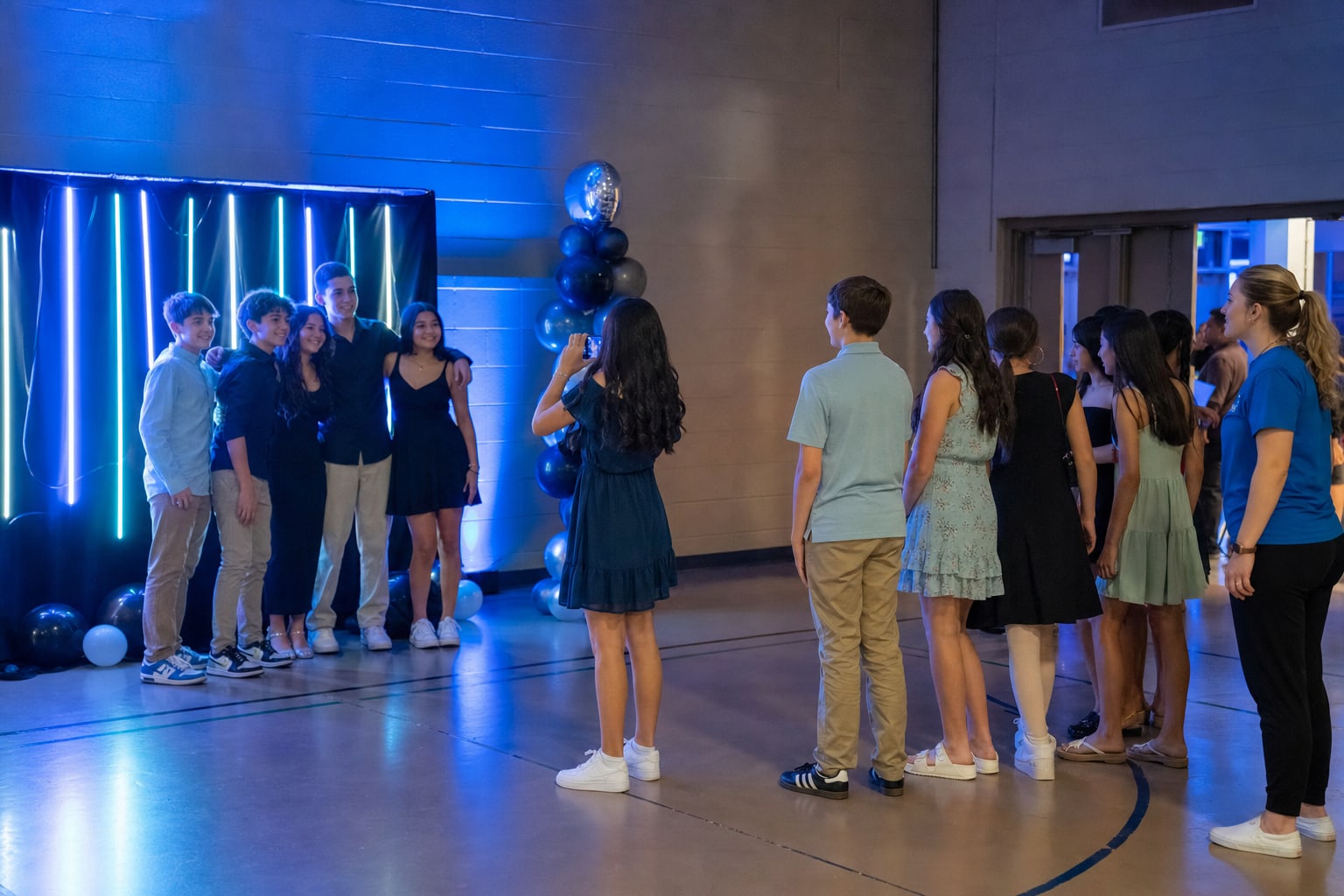Students taking turns at a blue-lit school dance photo backdrop while friends wait nearby
