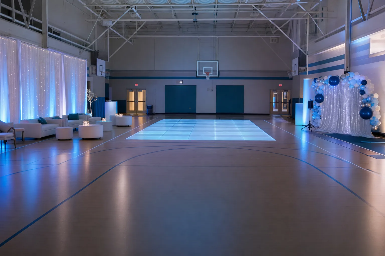 An empty school gym prepared for a dance with a glowing central floor, open walking paths, lounge seating, and a photo backdrop