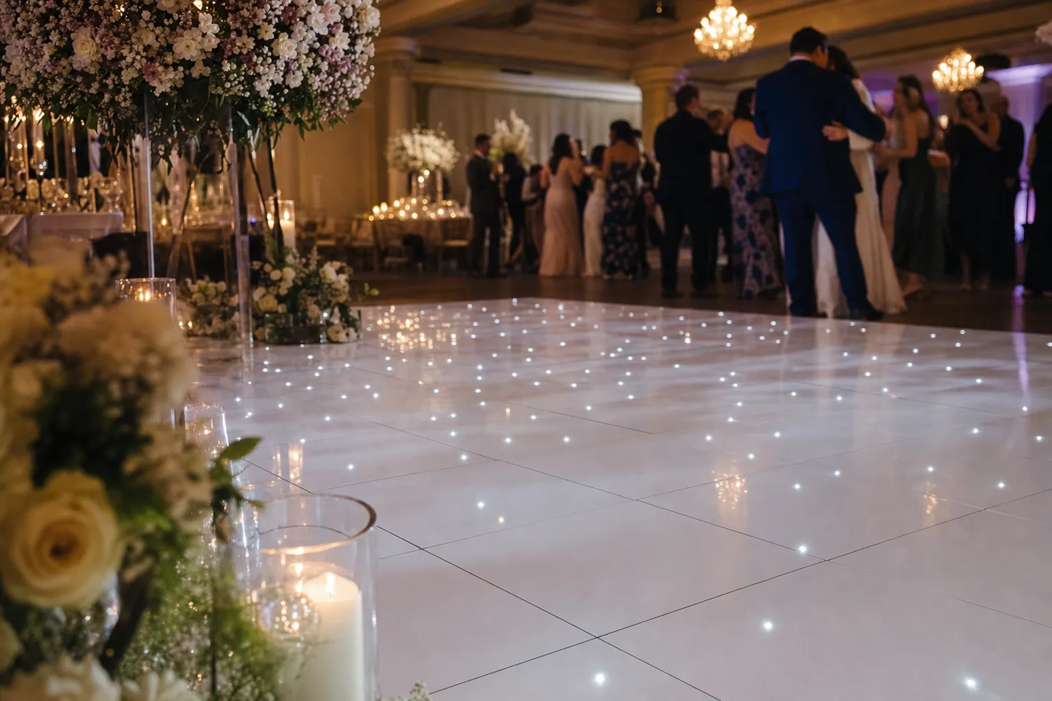 White LED dance floor reflecting candlelight and florals at a wedding reception