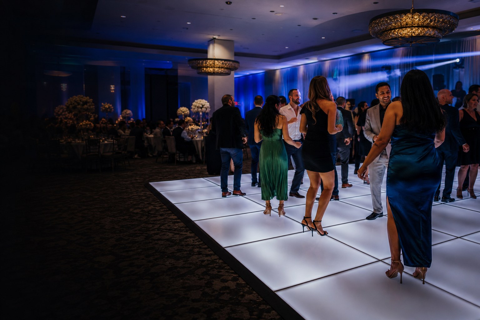 Guests gathered around a bright white illuminated dance floor at an indoor celebration