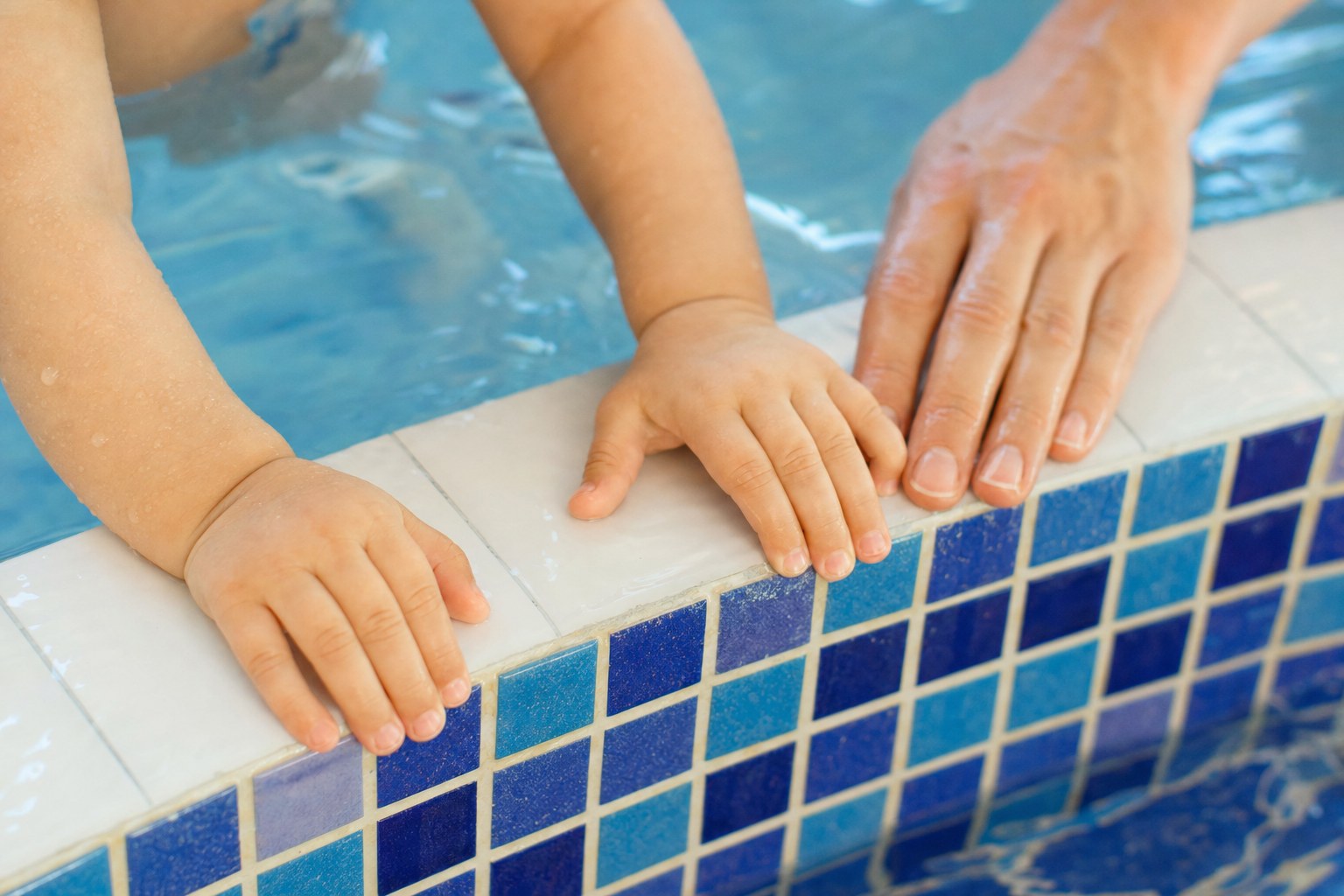 A child and adult holding the edge of an indoor pool